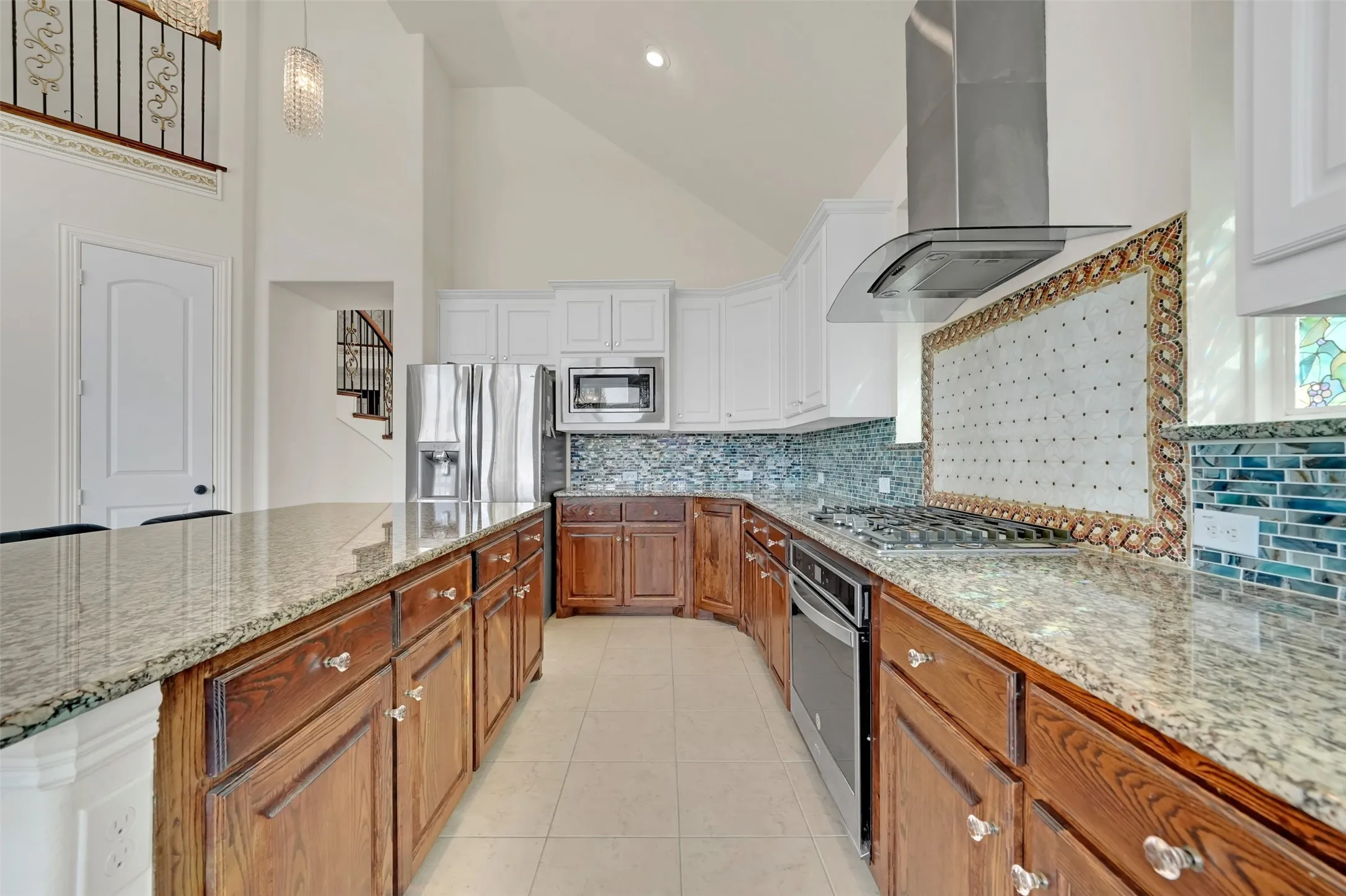 Kitchen featuring granite countertops, wood-finish lower cabinetry, white upper cabinetry, stainless steel appliances, and a mosaic tile backsplash