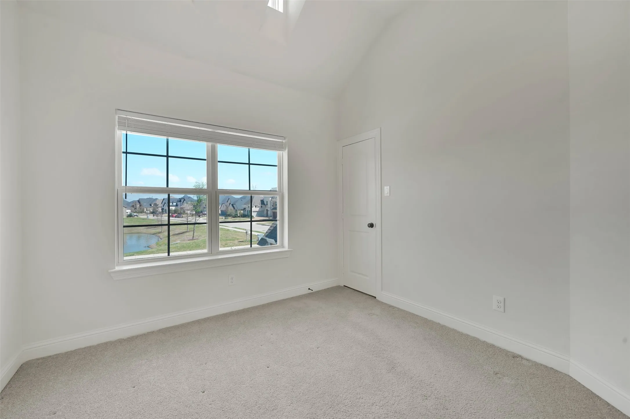 Carpeted room with vaulted ceiling and a window featuring horizontal blinds
