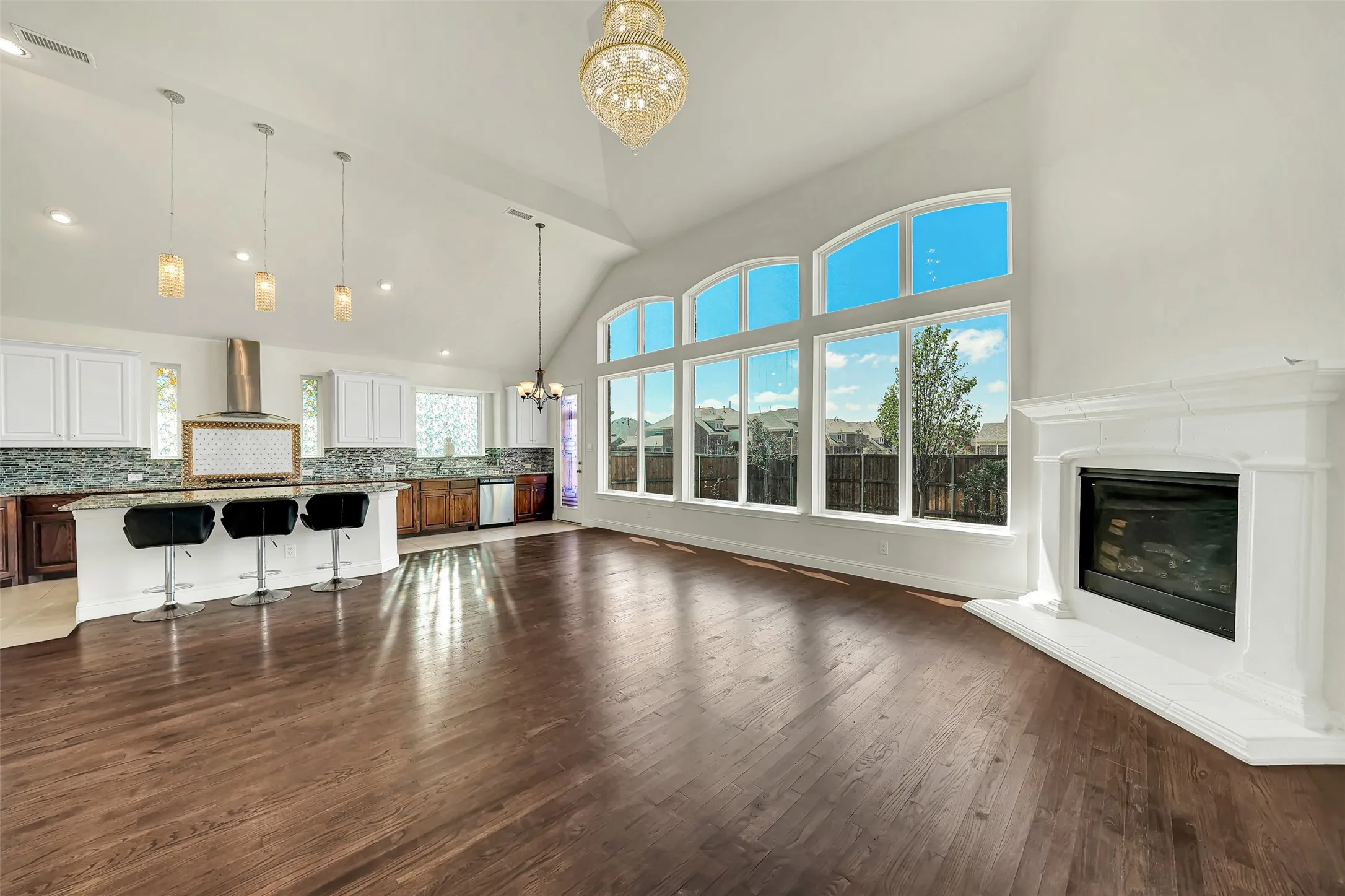 Vaulted ceiling with an ornate chandelier, expansive window wall with arched transoms, wood-finish flooring, and a corner fireplace