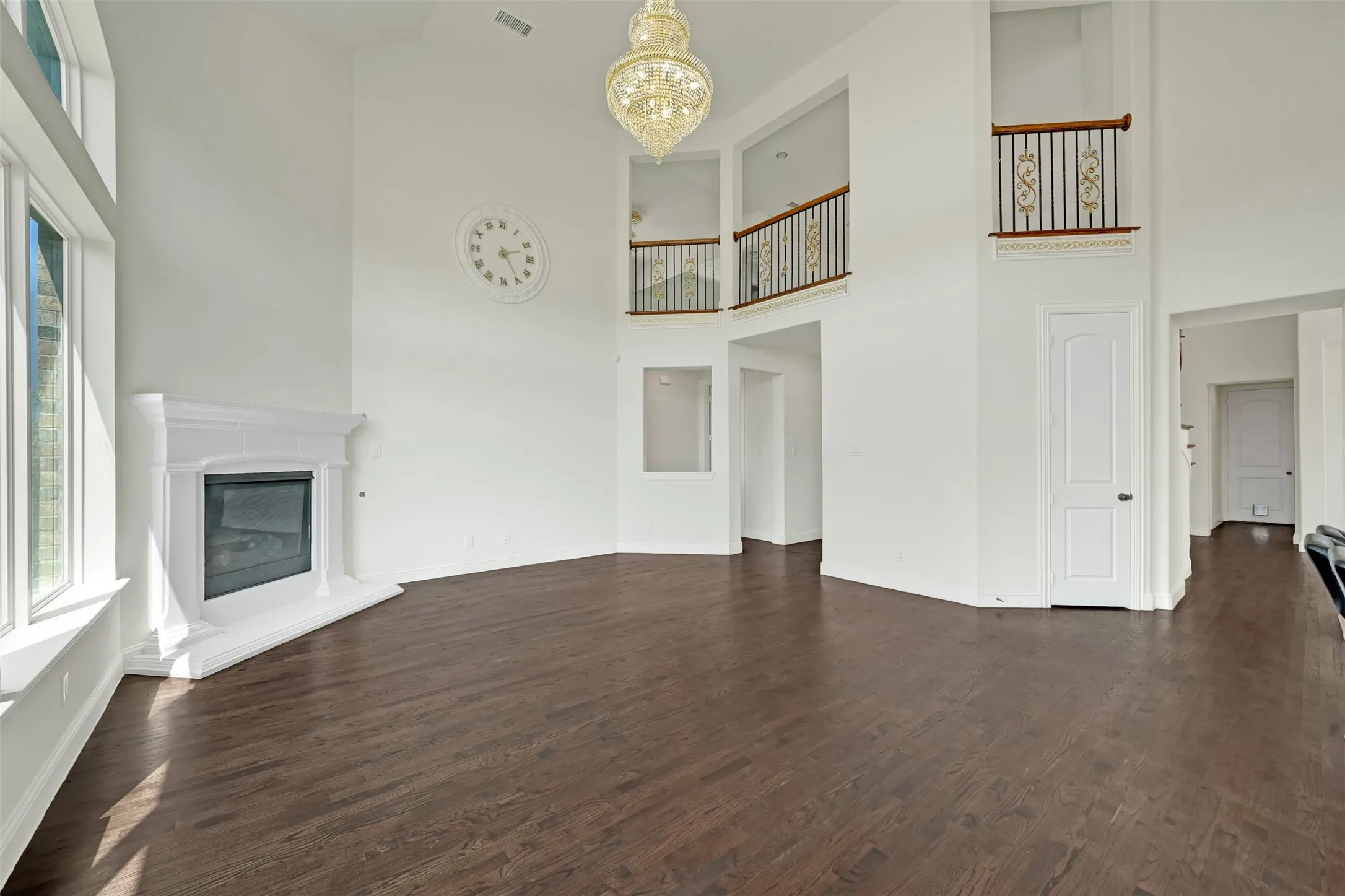 Hardwood flooring throughout, two-story ceiling, decorative chandelier, corner fireplace, and upper-level interior balconies with wrought iron railings