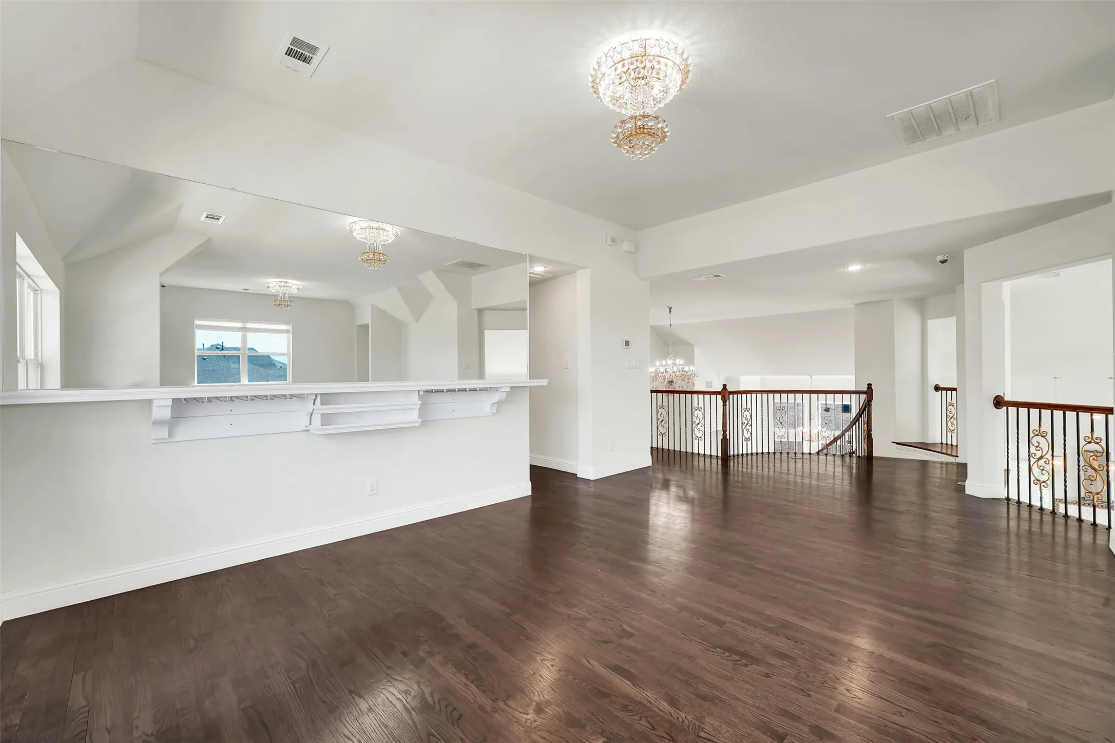 Dark wood-finish flooring, white walls, built-in mirrored wall, and wrought iron balusters