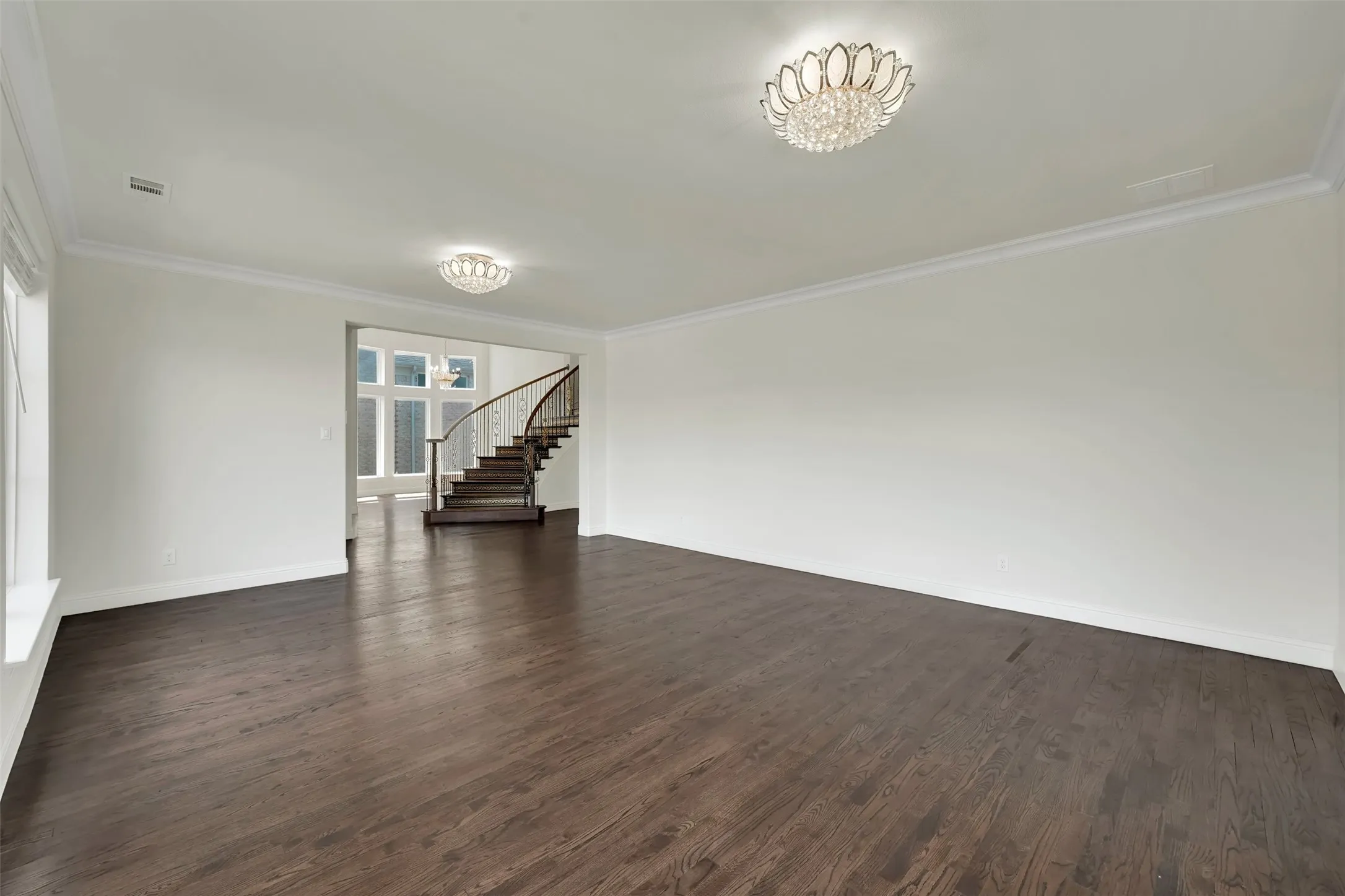 Hardwood flooring throughout, crown molding, two flush-mount crystal light fixtures, and a curved staircase with wood treads and a dark wood handrail