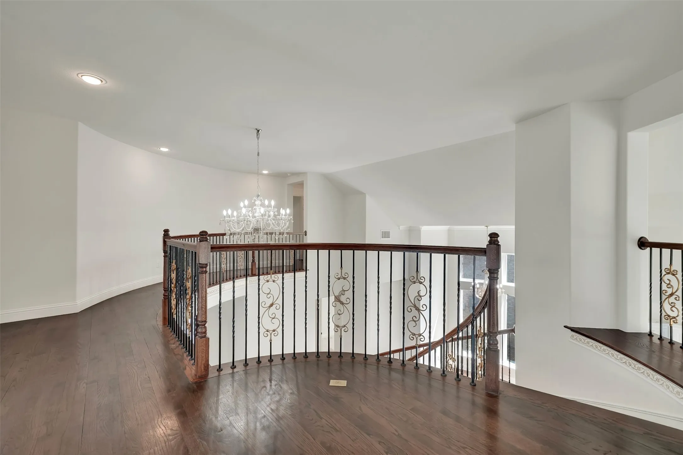 Hardwood flooring, wrought iron balusters with ornate details, recessed lighting, and a crystal chandelier