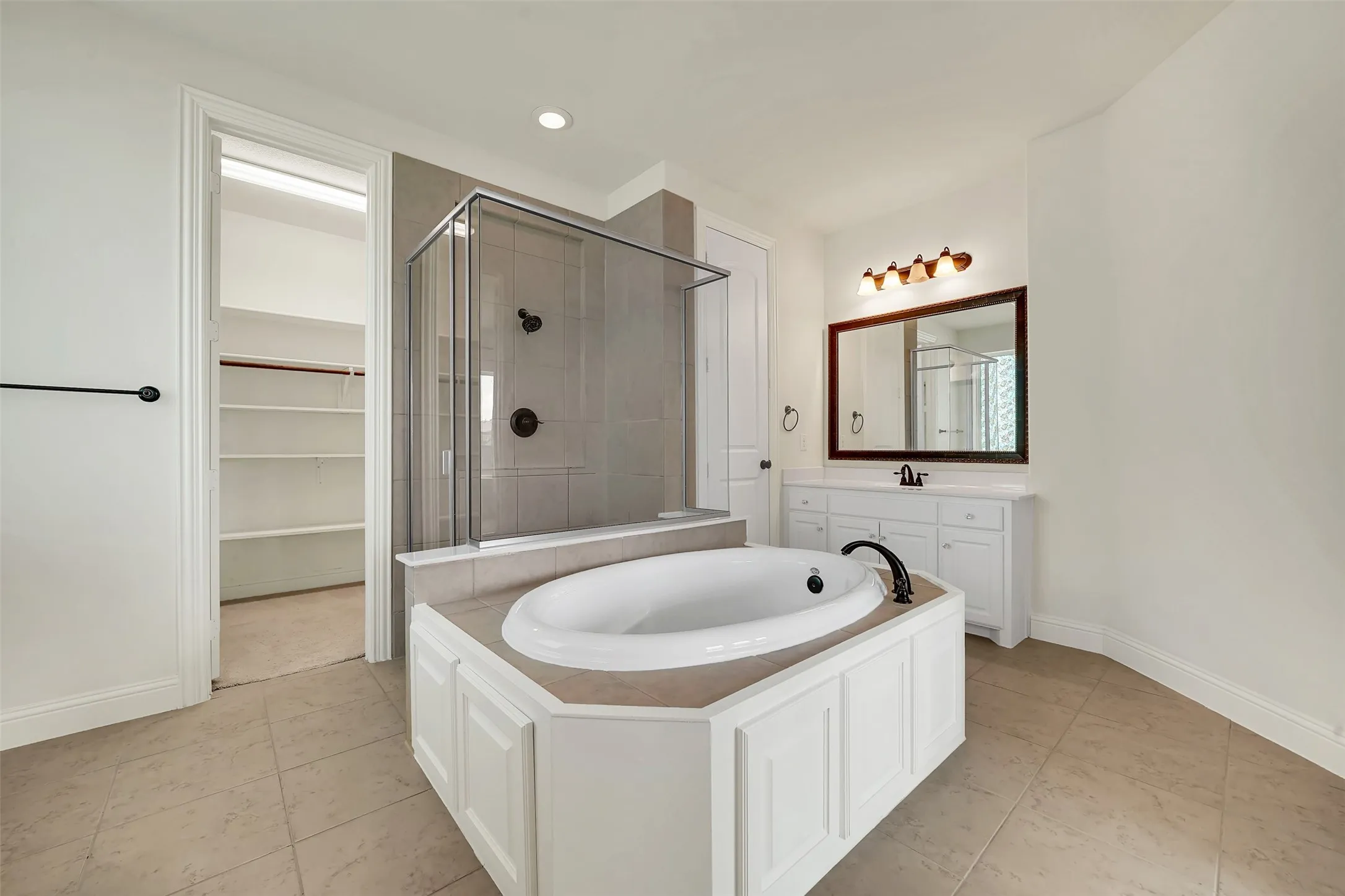 Soaking tub with a tiled surround, glass-enclosed shower, white vanity with a dark countertop, and tiled flooring