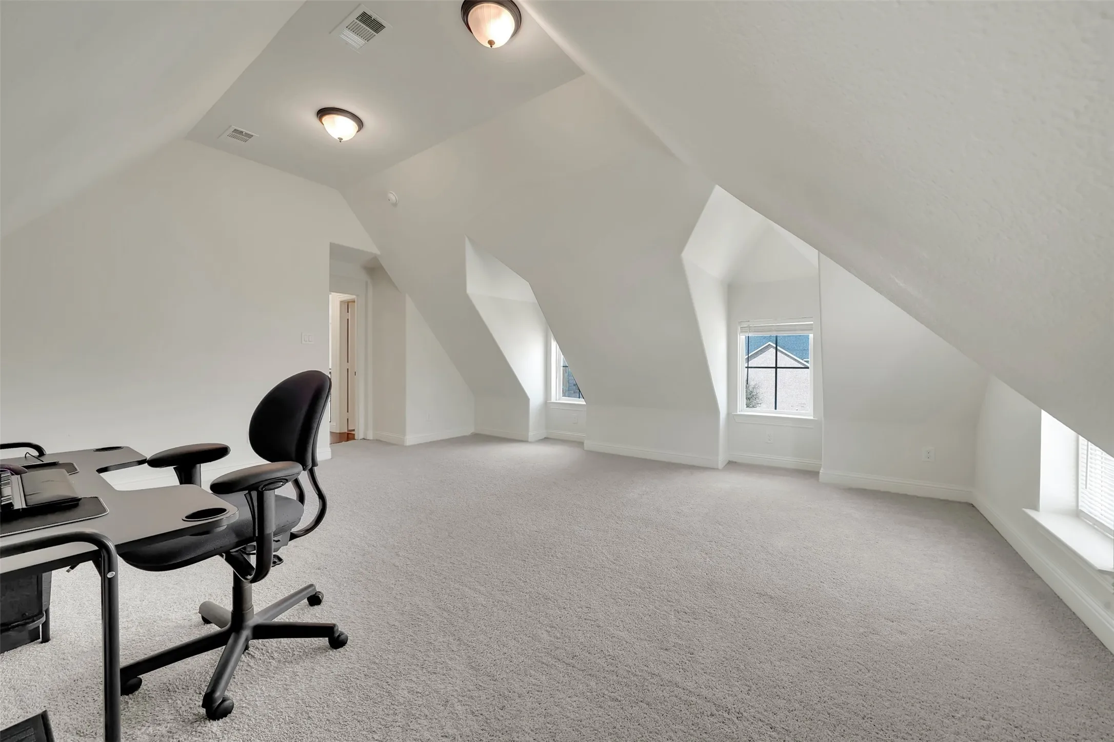 Spacious attic room featuring sloped ceilings, recessed dormer windows with blinds, light-toned carpeting, and flush-mount ceiling lights