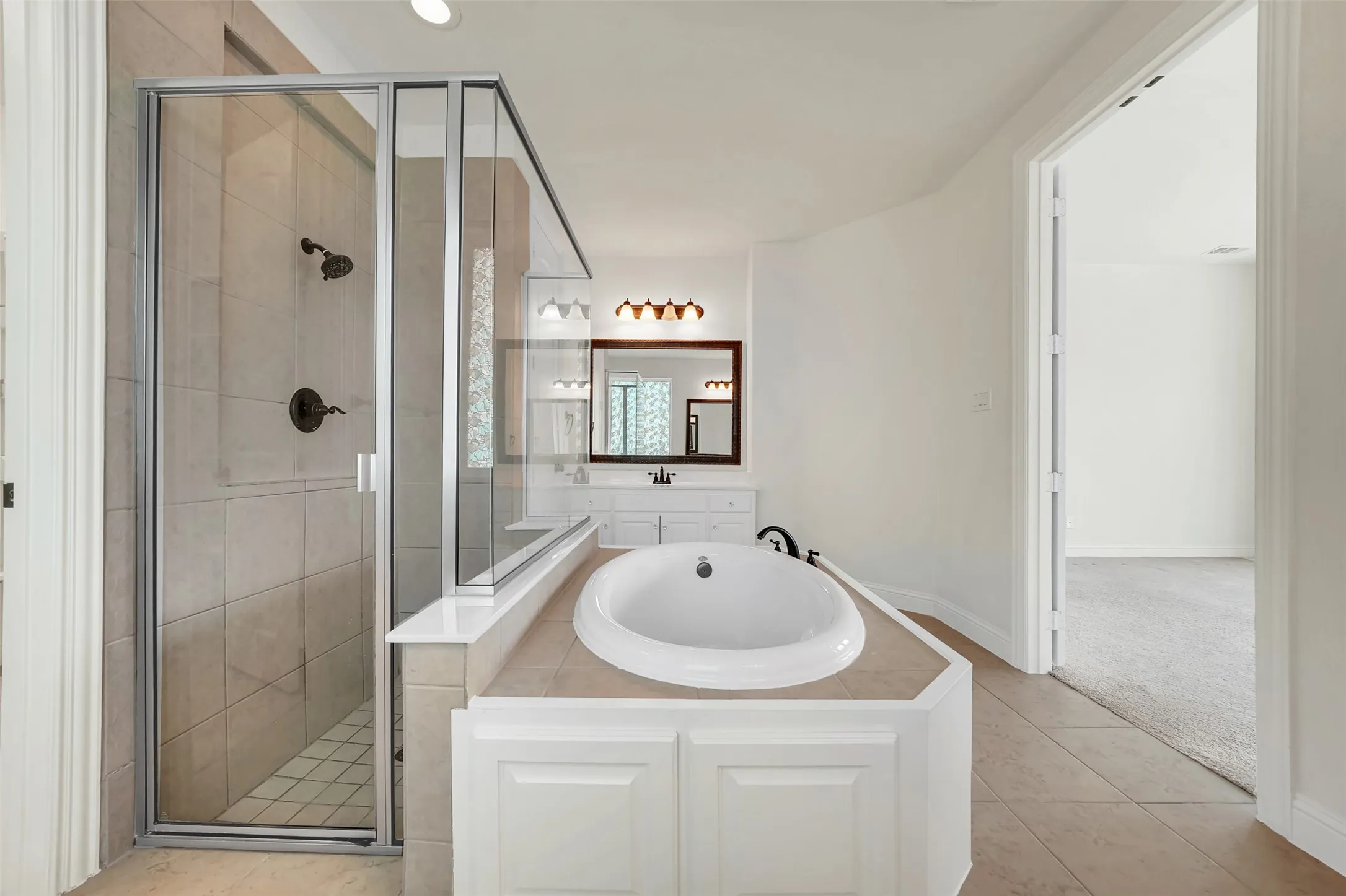 Built-in soaking tub, walk-in shower with glass enclosure, white paneled vanity, and recessed lighting