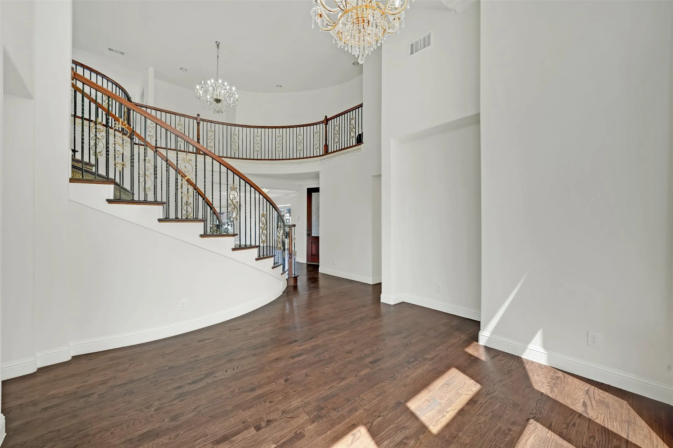 Grand two-story entry with a curved staircase, wrought iron balusters, wood-finish flooring, and two chandelier light fixtures