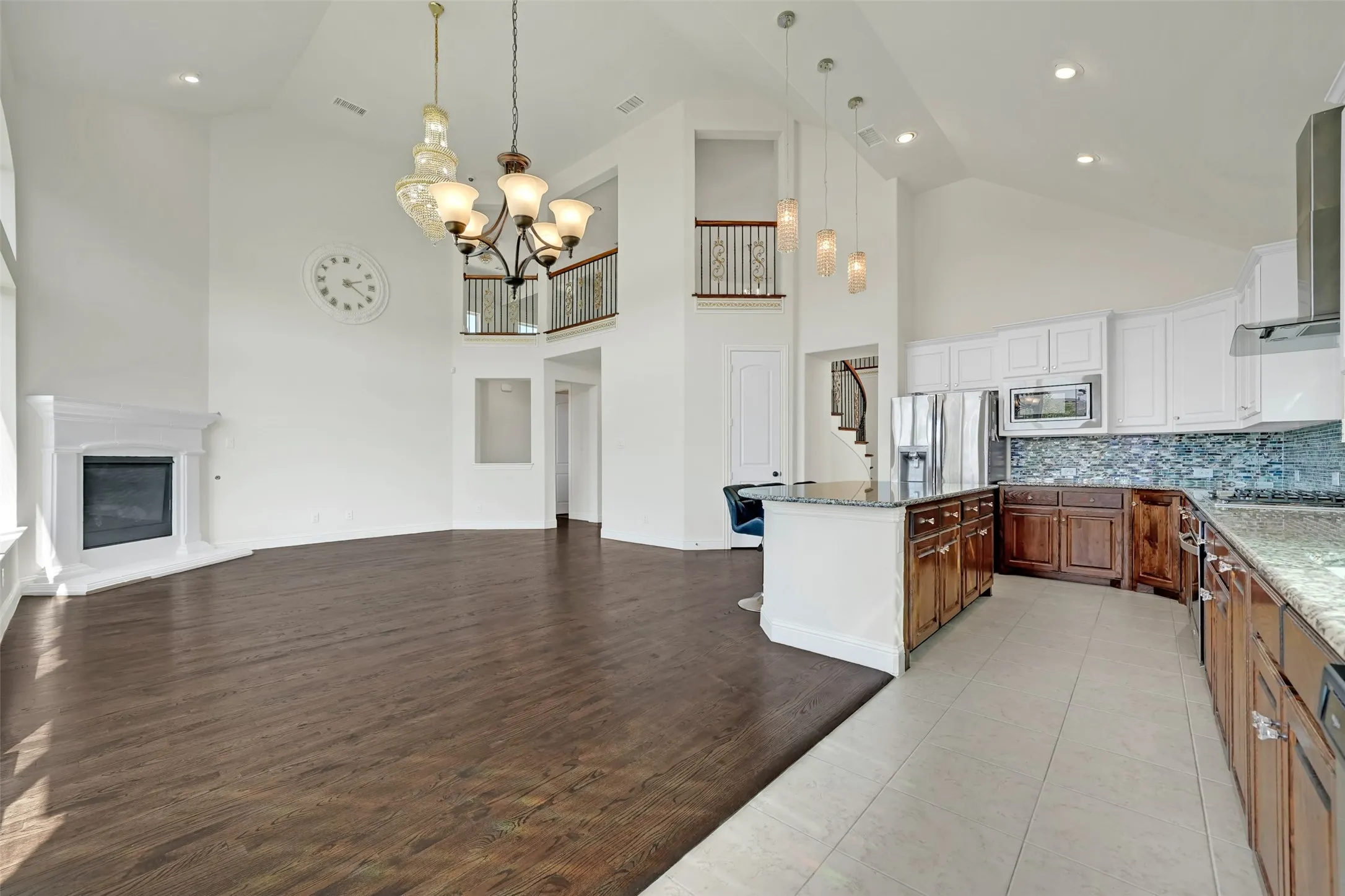 Vaulted ceilings with recessed lighting, a corner fireplace with a white mantel, wood-finish flooring, and a kitchen island with built-in cabinetry