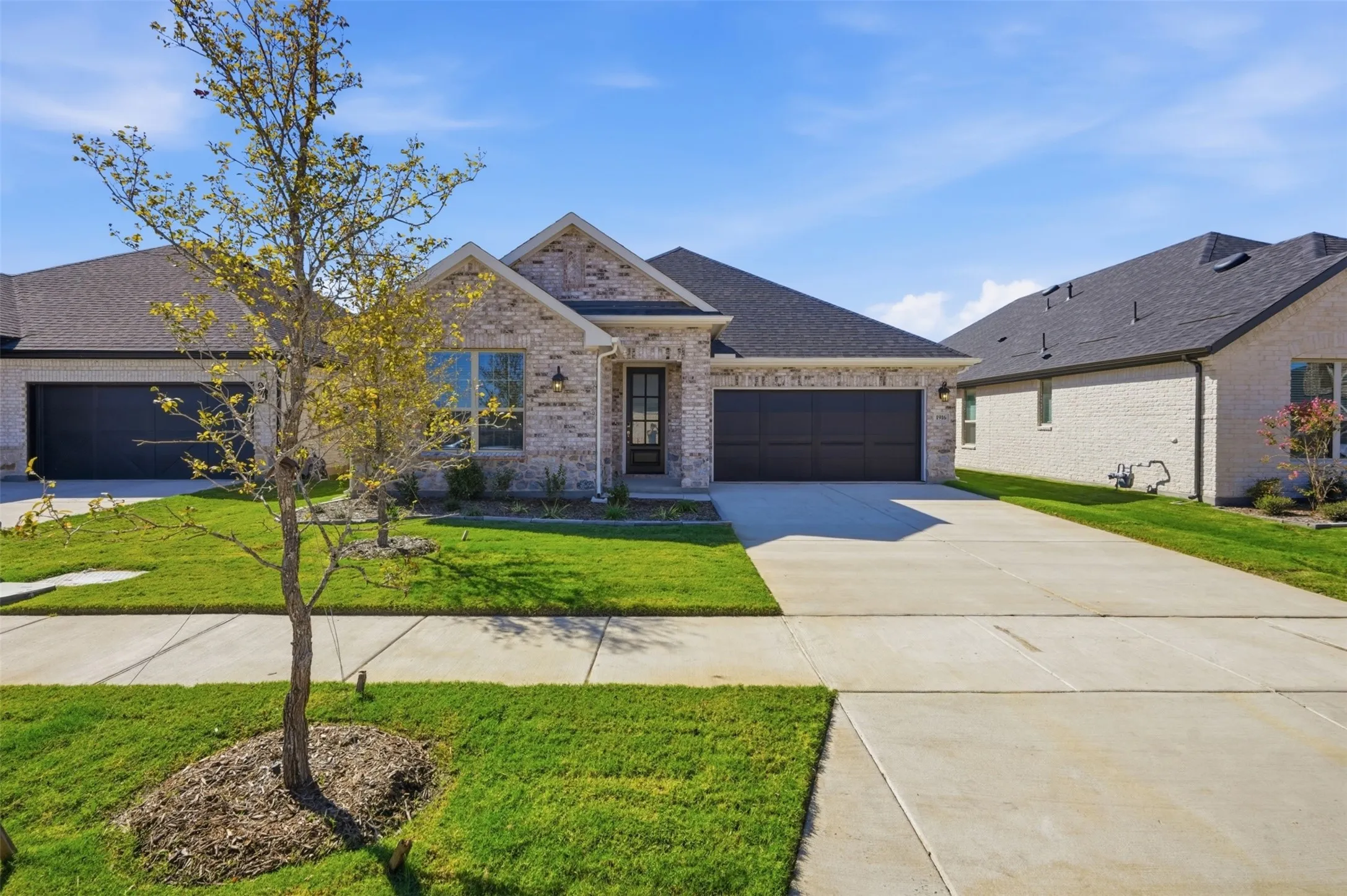 Brick façade with dark trim accents, attached two-car garage, concrete driveway, and front lawn