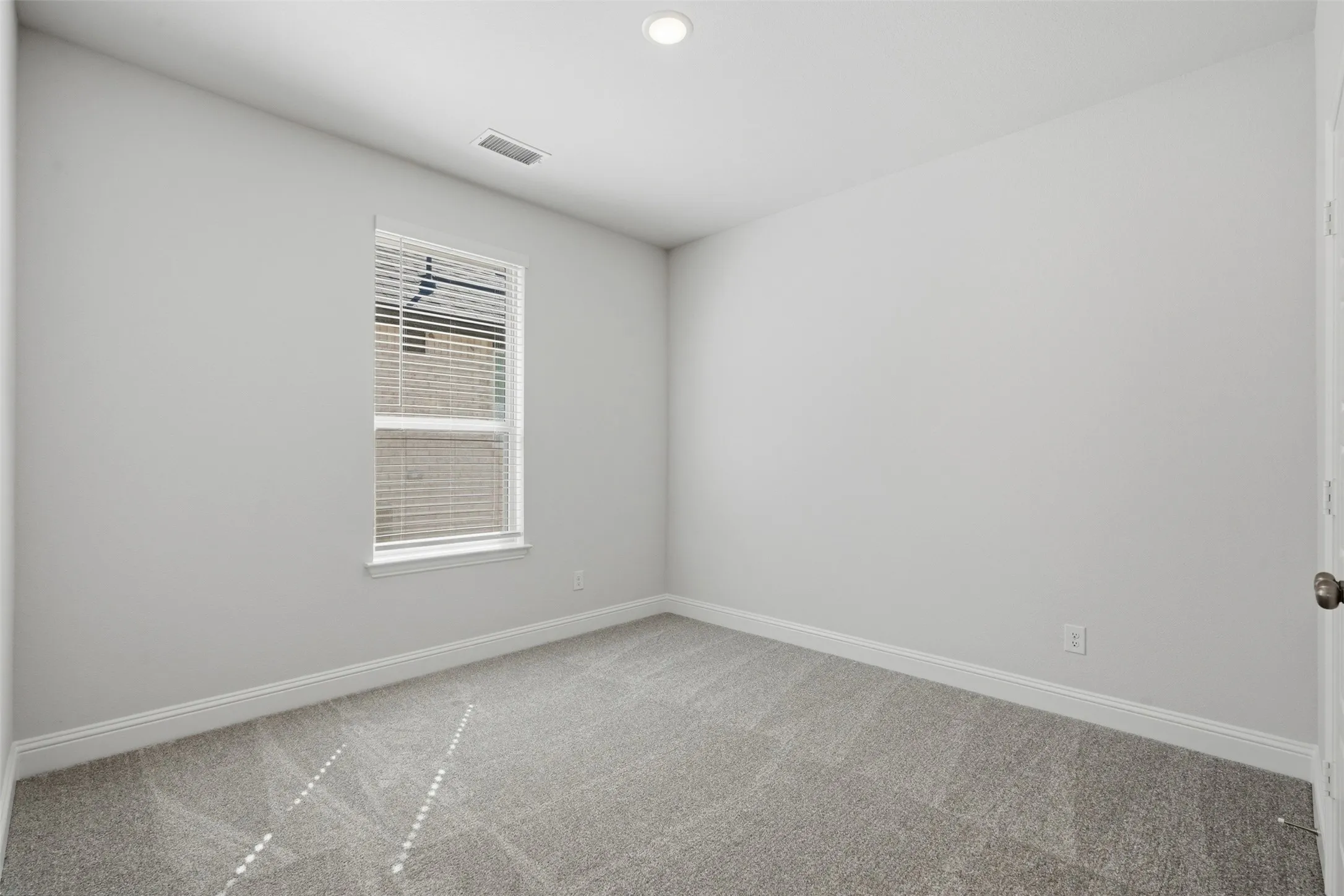 Recessed ceiling lighting illuminates a room featuring light gray carpeting and white painted walls
