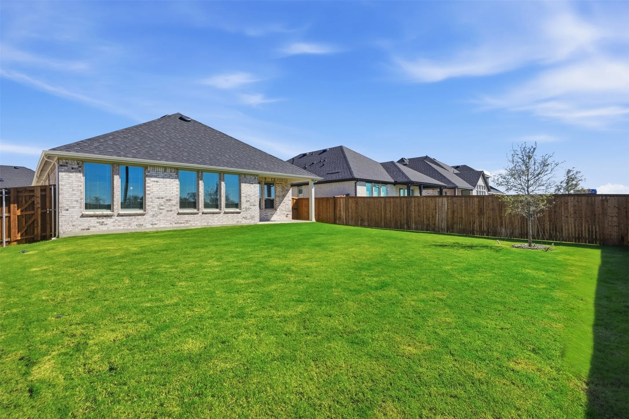 Expansive lawn featuring a privacy fence, a mature tree, and a light-colored brick exterior