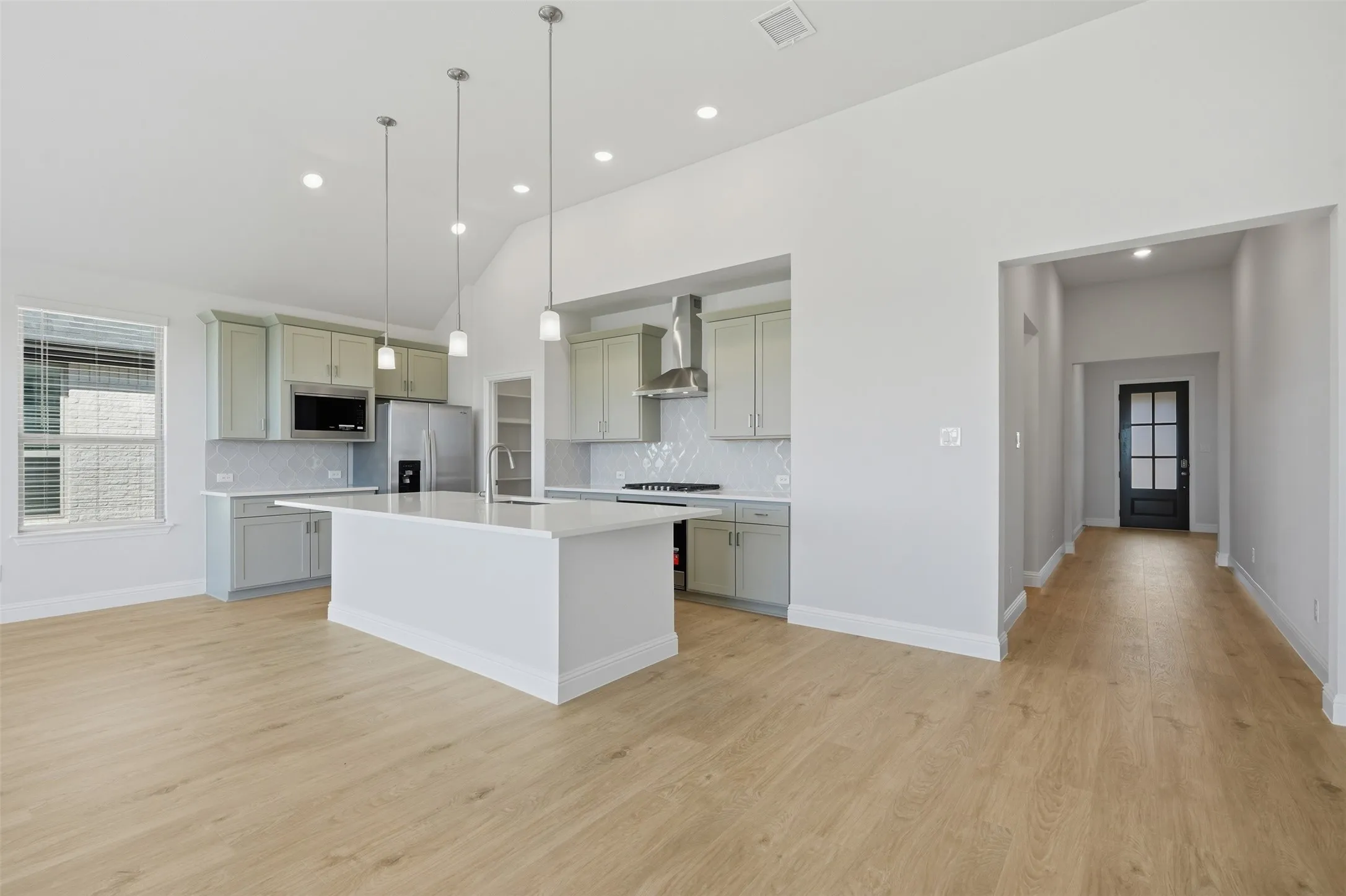 Vaulted ceiling, recessed lighting, wood-finish flooring, central kitchen island, and light-toned cabinetry
