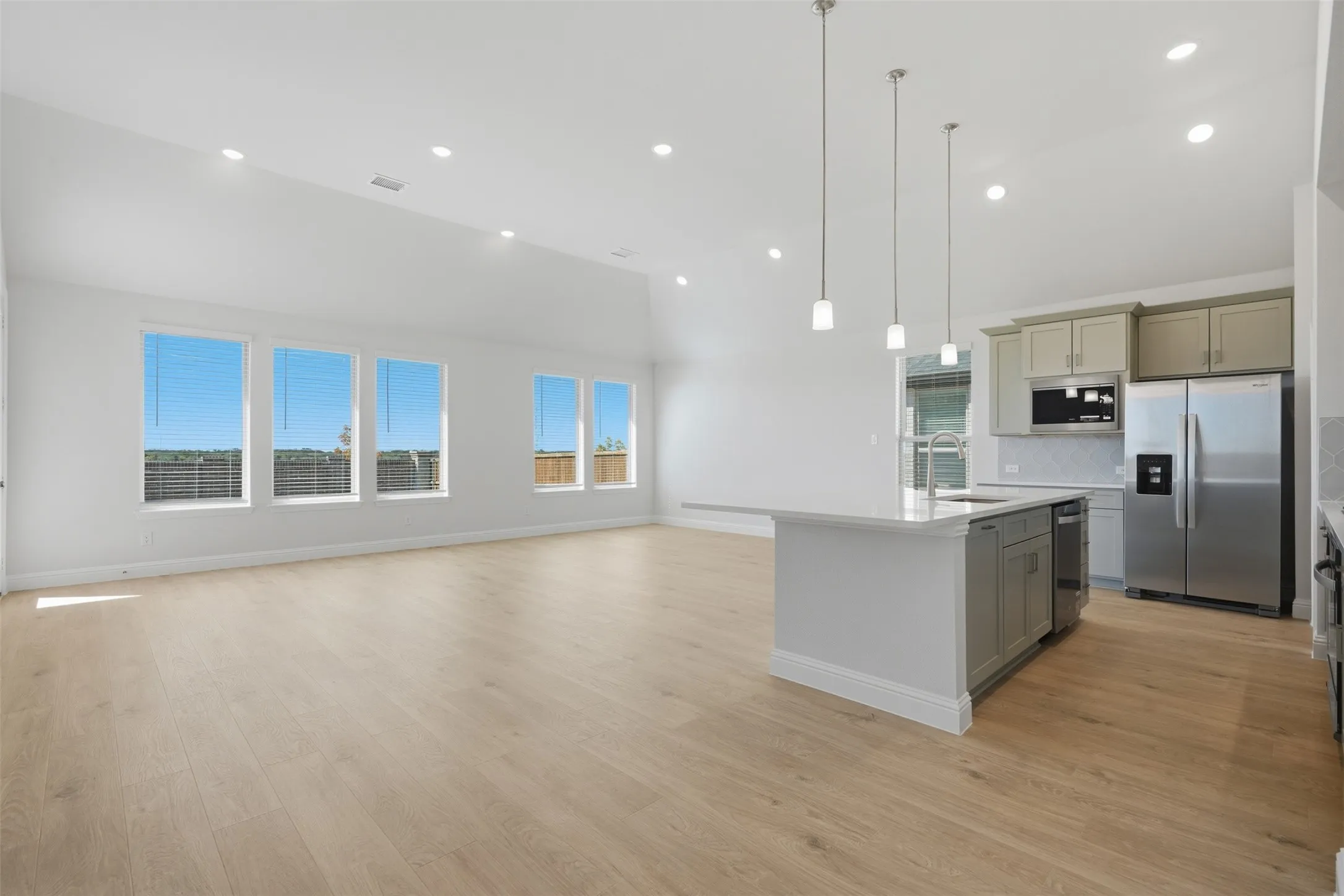 Open-concept living space with wood-finish flooring, vaulted ceilings, recessed lighting, and large windows