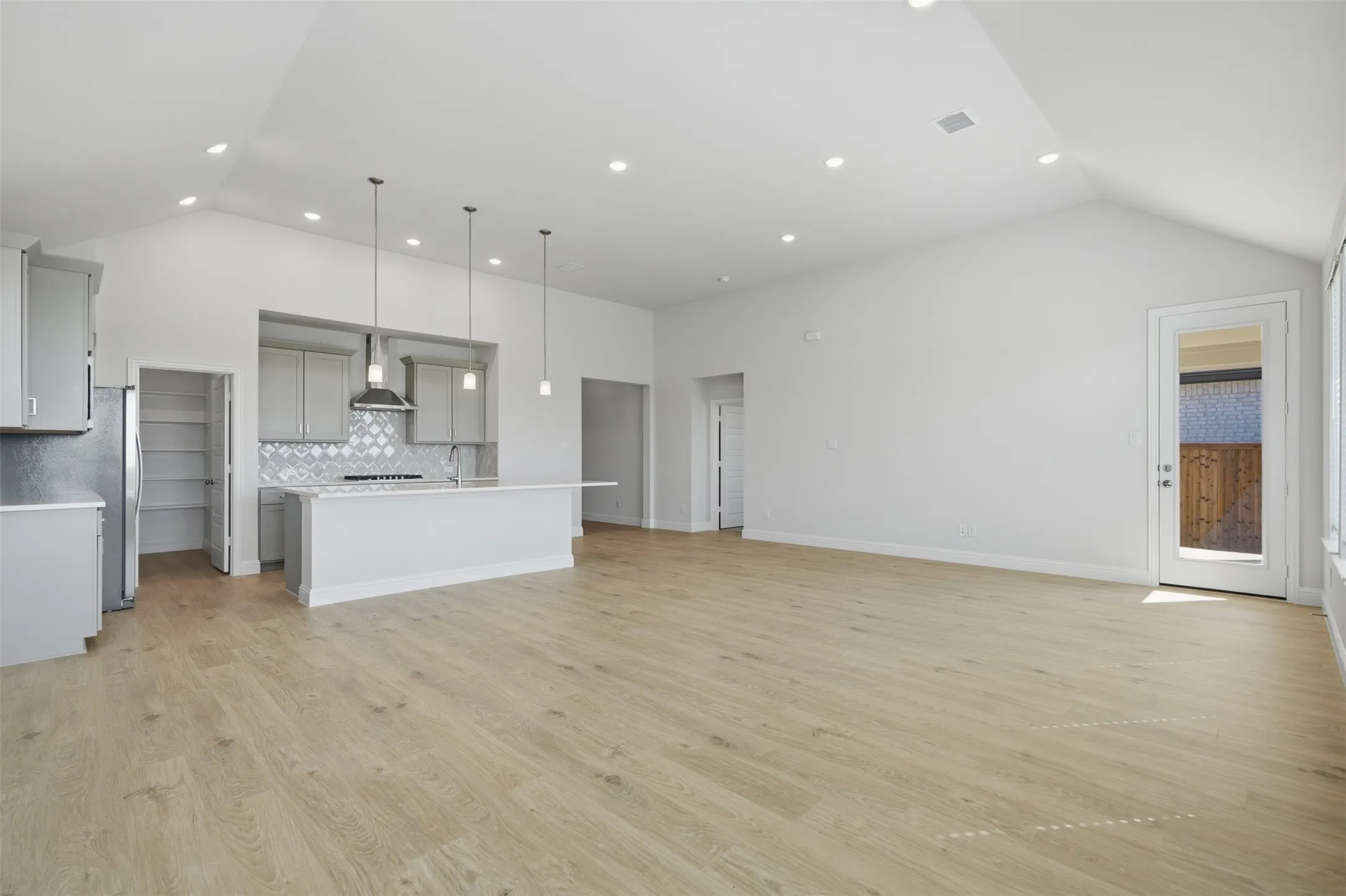 Open-concept living area with vaulted ceilings, wood-finish flooring, recessed lighting, and a glass-paneled door