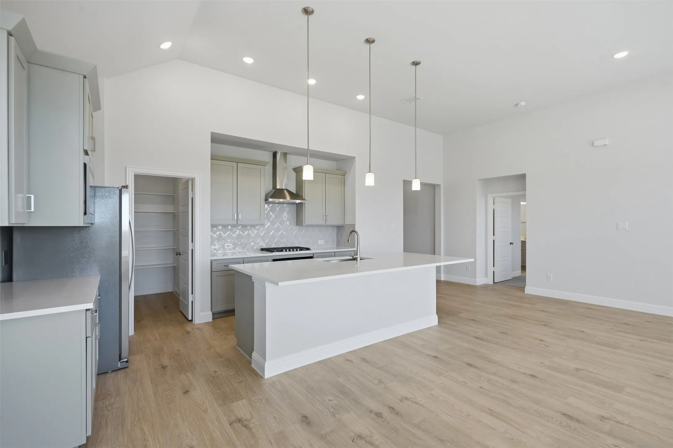 Vaulted ceiling with recessed lighting, light wood-finish flooring, central island with pendant lighting, stainless steel appliances, and a tiled backsplash