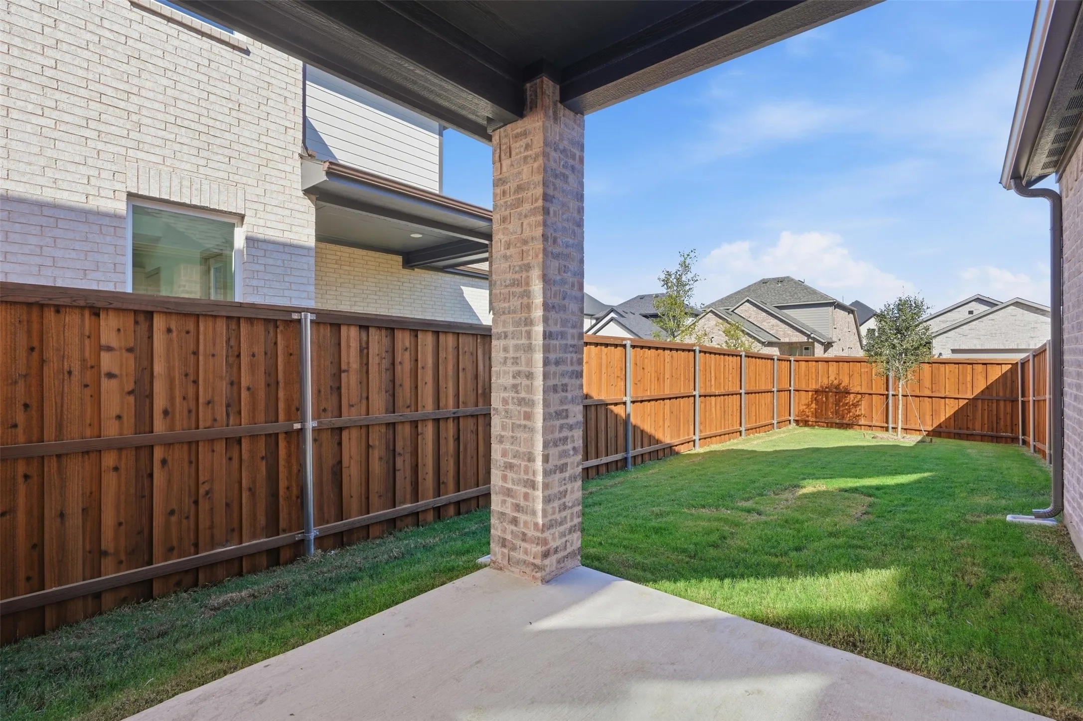 Covered patio area with brick support column, concrete flooring, and a private fenced yard with natural grass