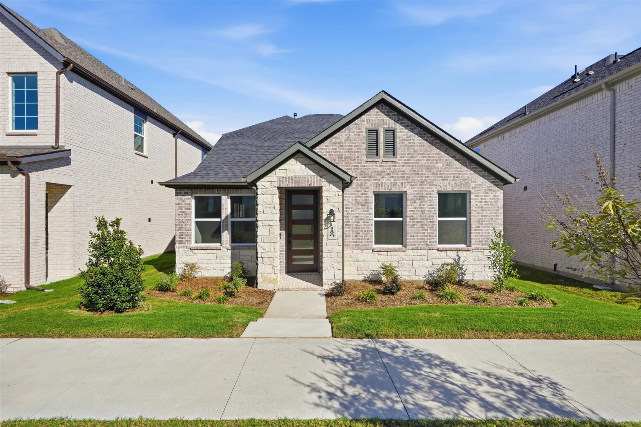 Brick and stone veneer exterior with a dark shingle roof, featuring a modern entry door with horizontal lites, and framed windows