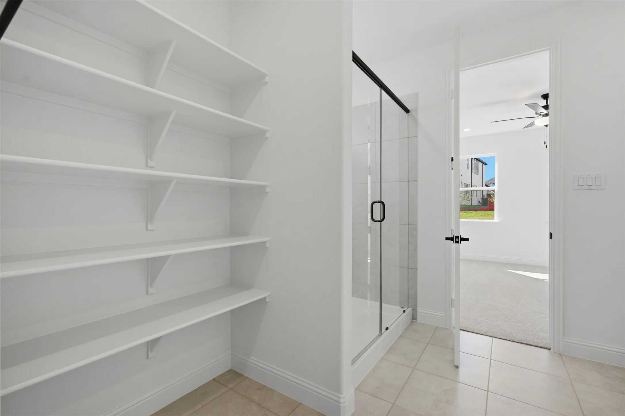 Built-in shelving, glass-enclosed shower with black trim, and light tile flooring