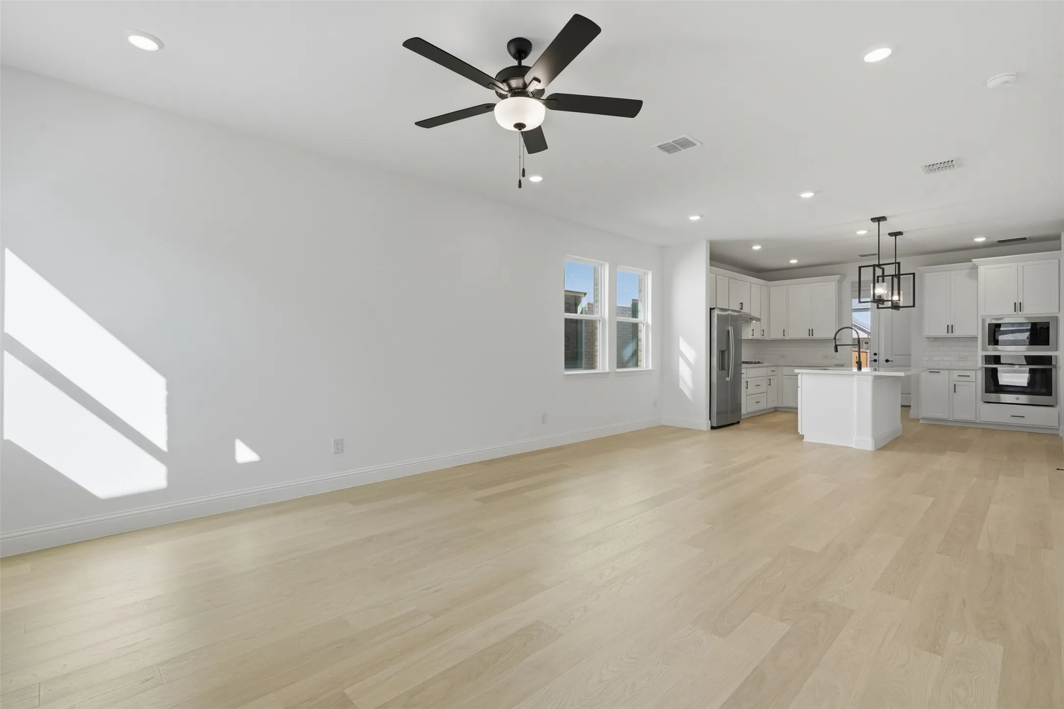 Open-concept living space with light wood-finish flooring, recessed lighting, and a modern ceiling fan