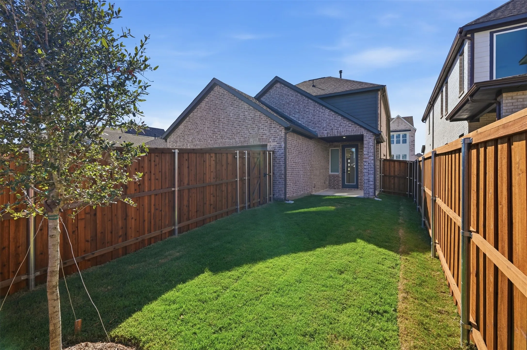 Expansive backyard featuring a manicured lawn, wood fencing, and a covered patio area