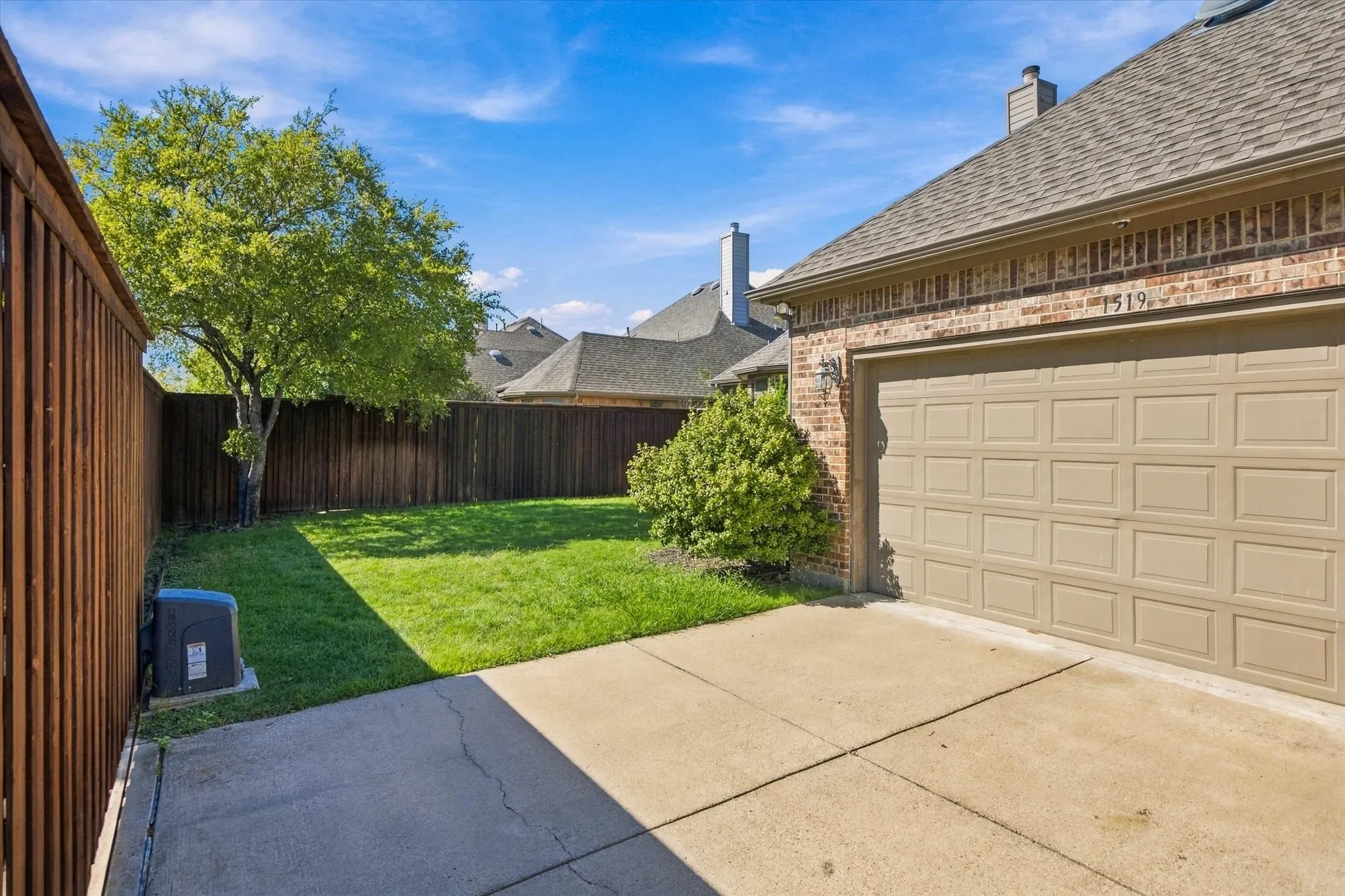 Brick exterior with a two-car garage, concrete driveway, and a fenced backyard with a lawn