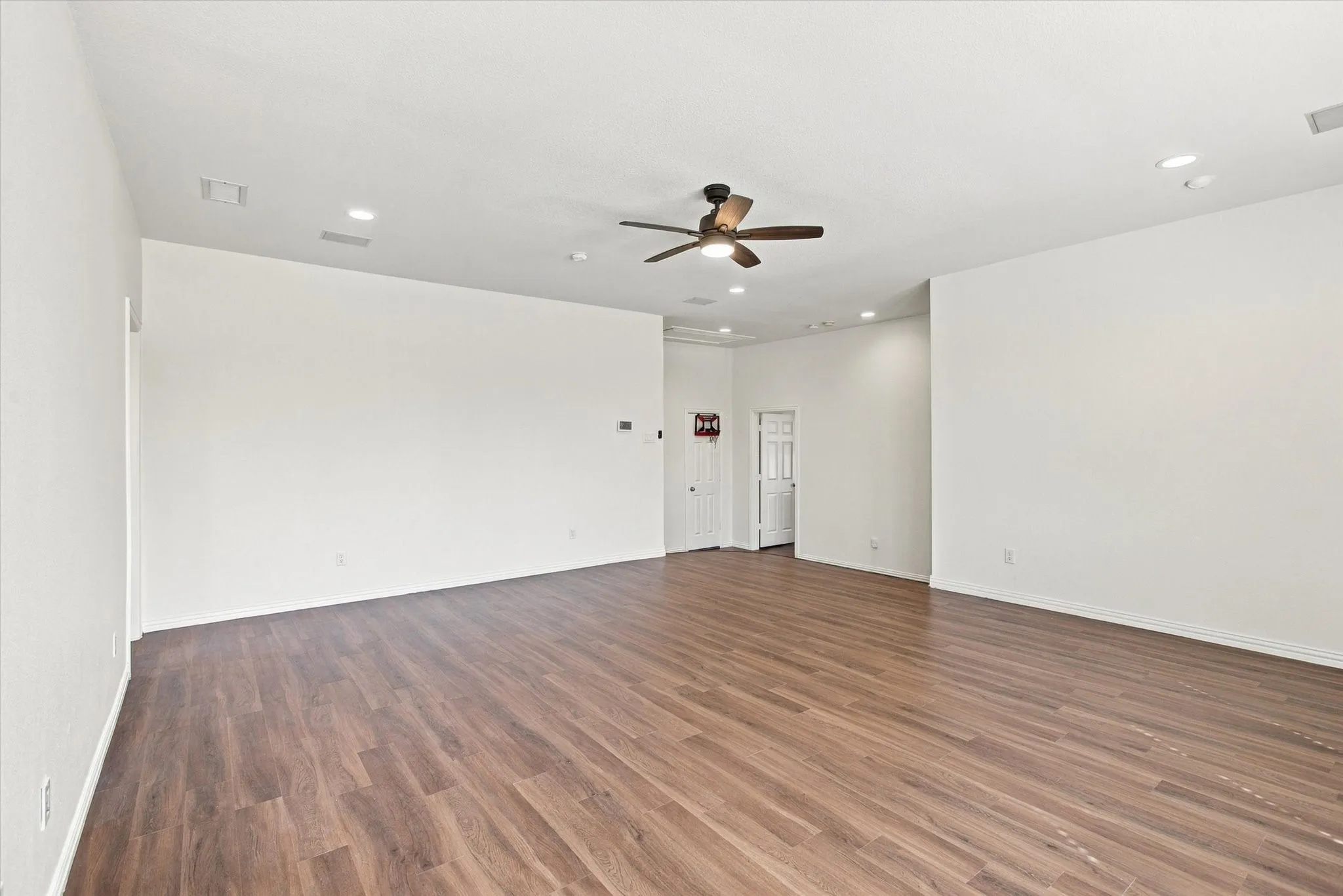 Spacious room featuring wood-finish flooring, recessed lighting, and a ceiling fan