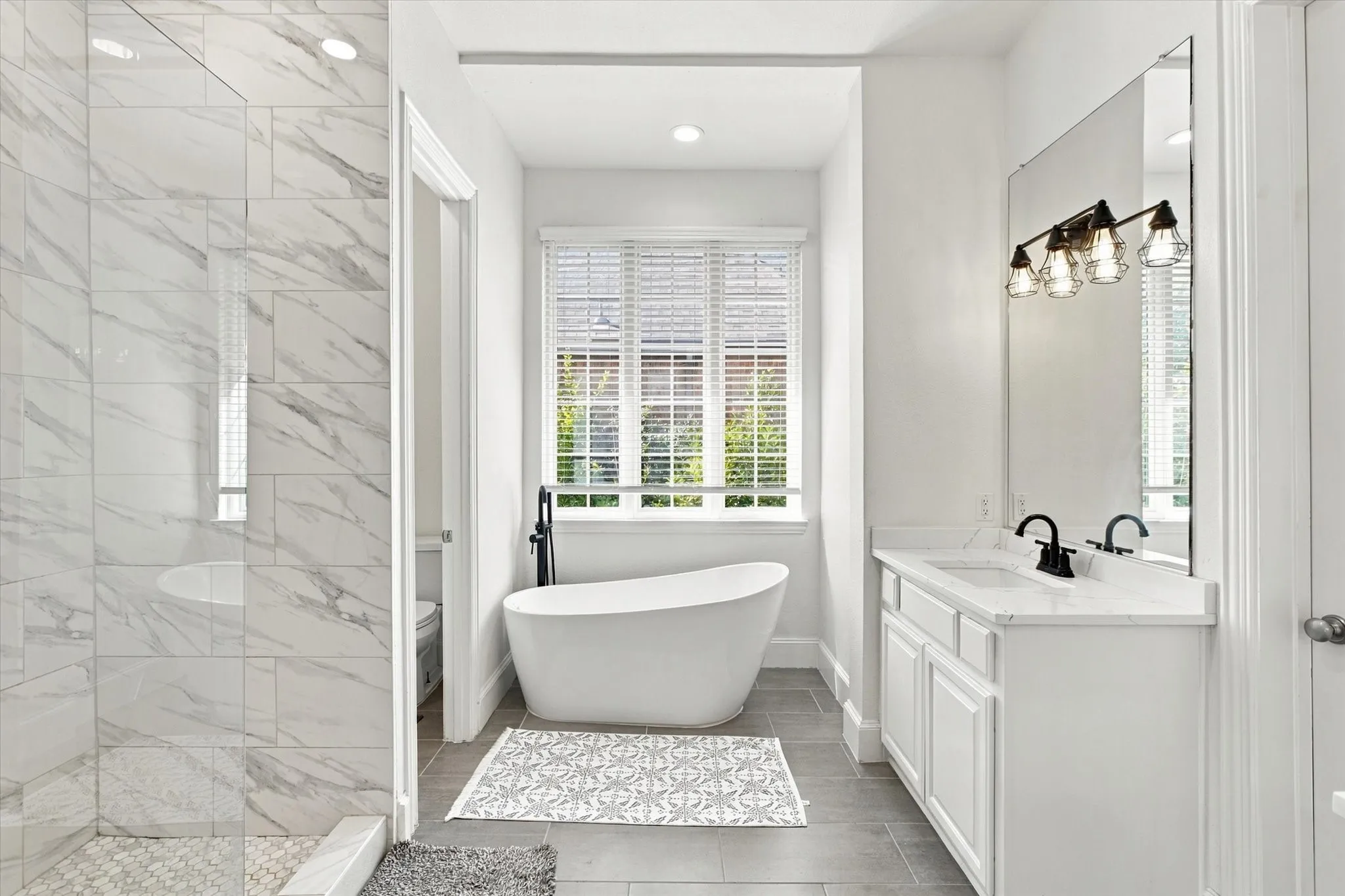 Freestanding soaking tub, dual vanity with undermount sinks, full-height mirror, and a tiled shower with glass enclosure