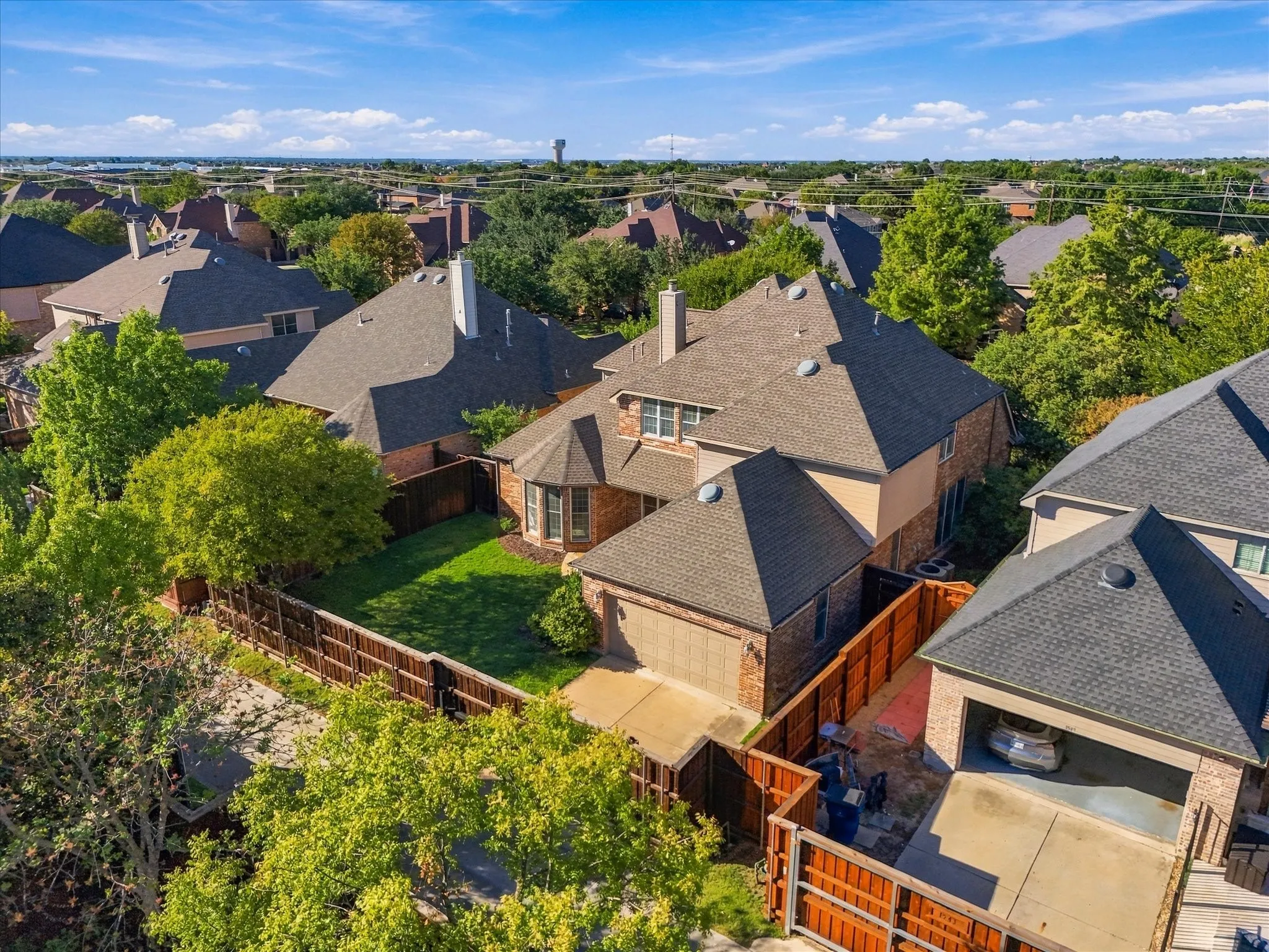 Brick exterior with a peaked roofline, attached garage, and a fenced backyard with green space
