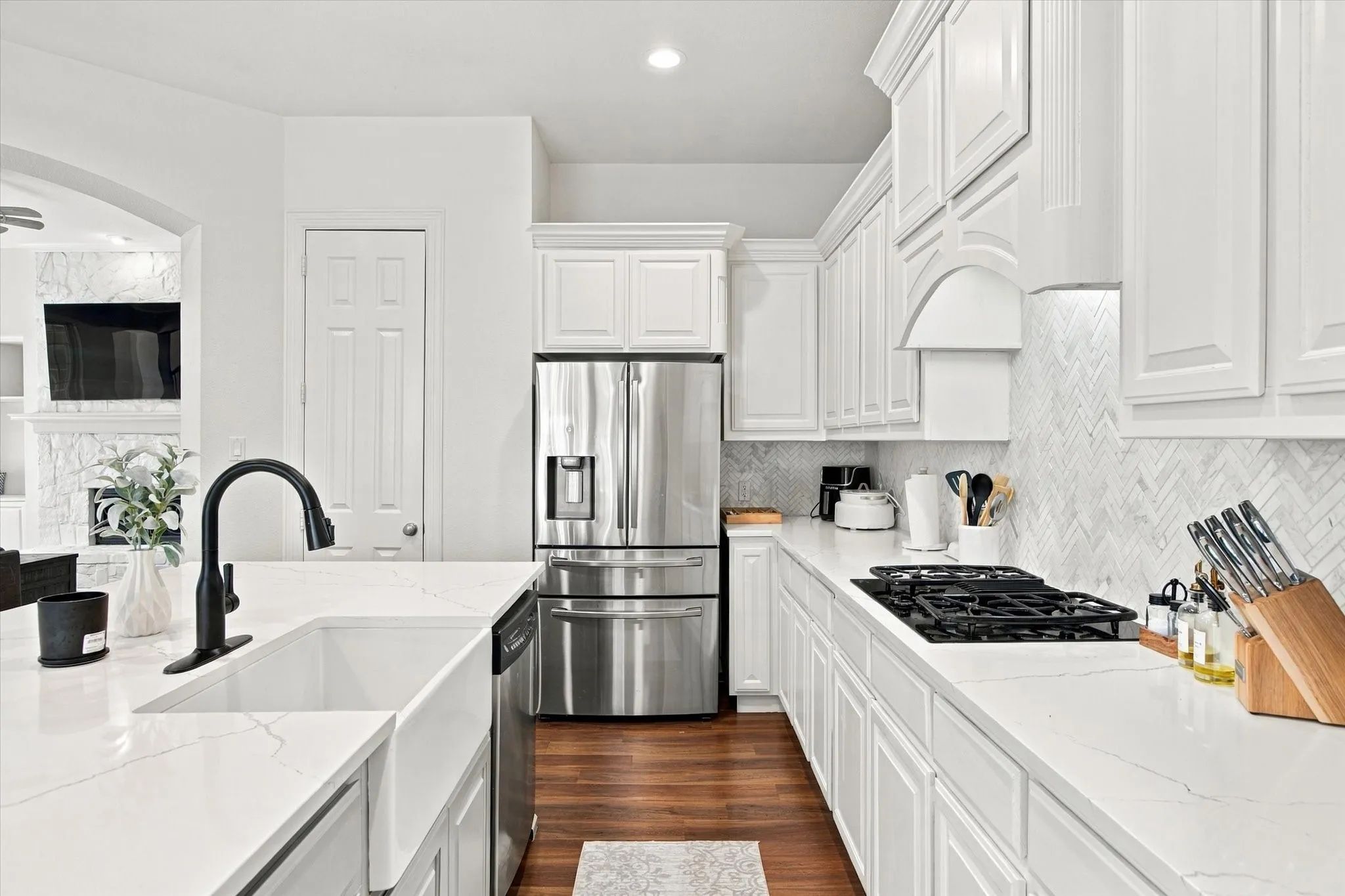 White shaker cabinetry, stainless steel appliances, white quartz countertops, herringbone tile backsplash, and wood-finish flooring