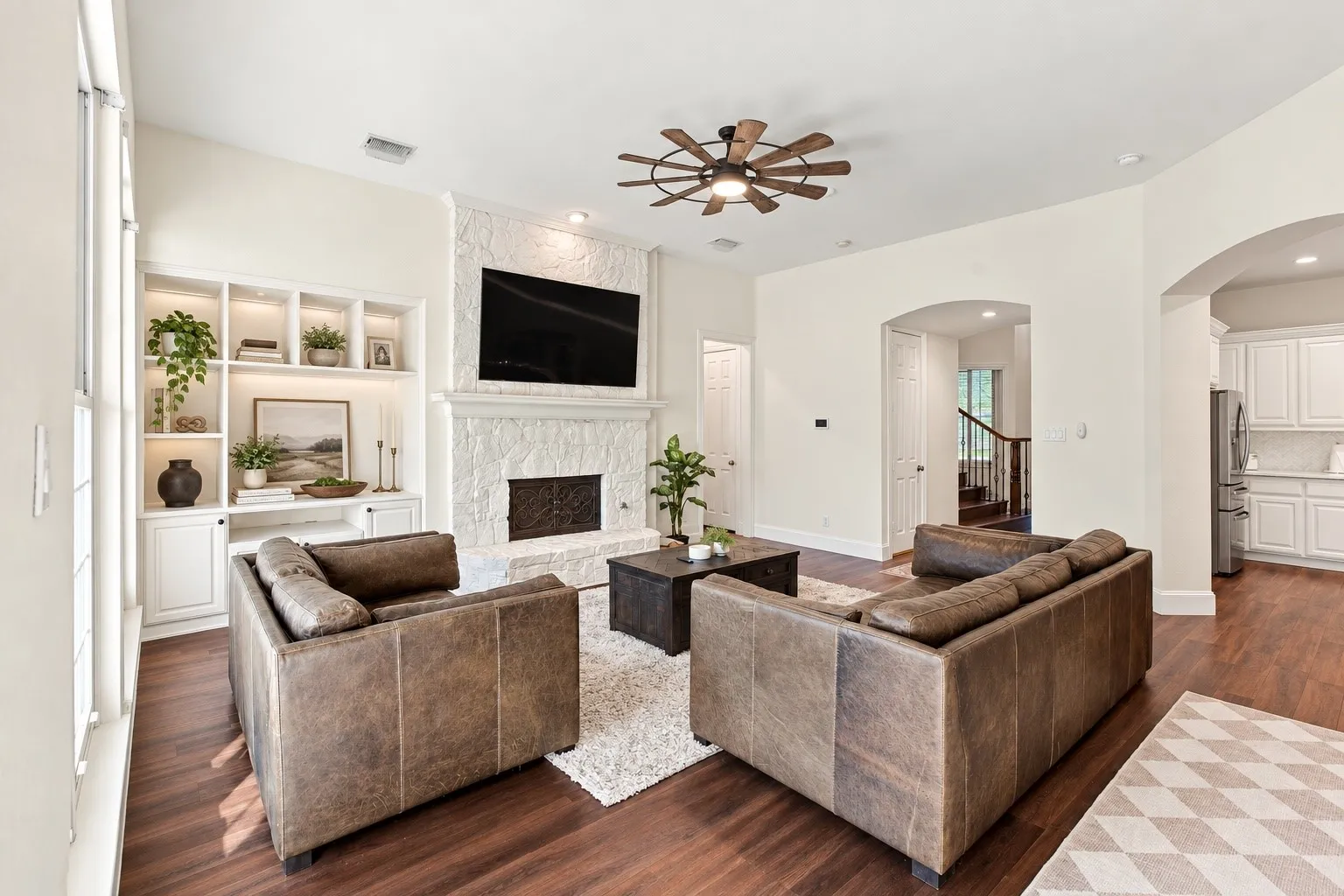 Living area featuring wood-finish flooring, white built-in shelving with integrated lighting, a stone fireplace, and an arched entryway