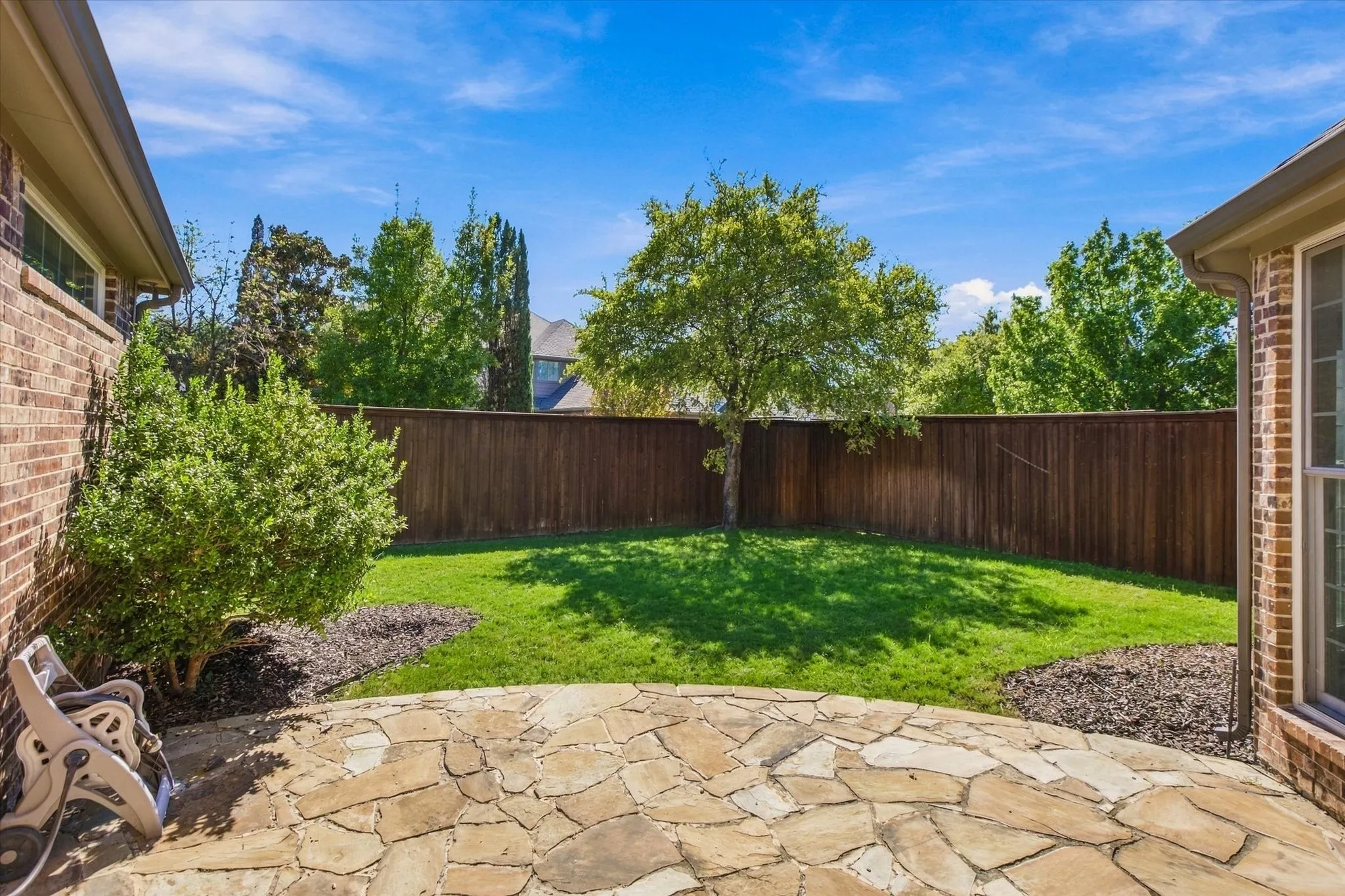 Expansive backyard featuring a natural stone patio, manicured lawn, and privacy fencing