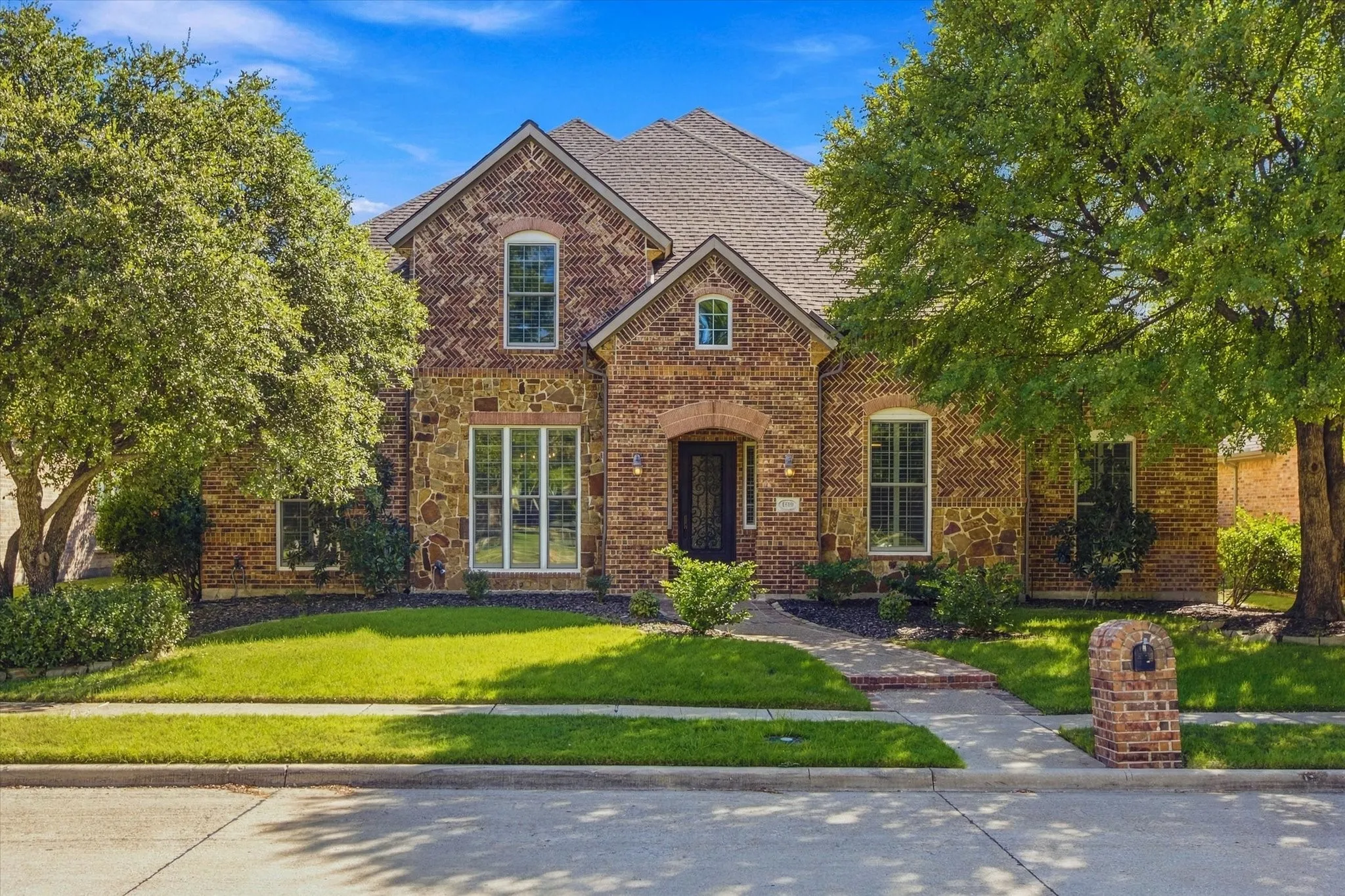 Brick and stone facade with arched entry, gabled roofline, multiple window styles, and a brick-clad mailbox