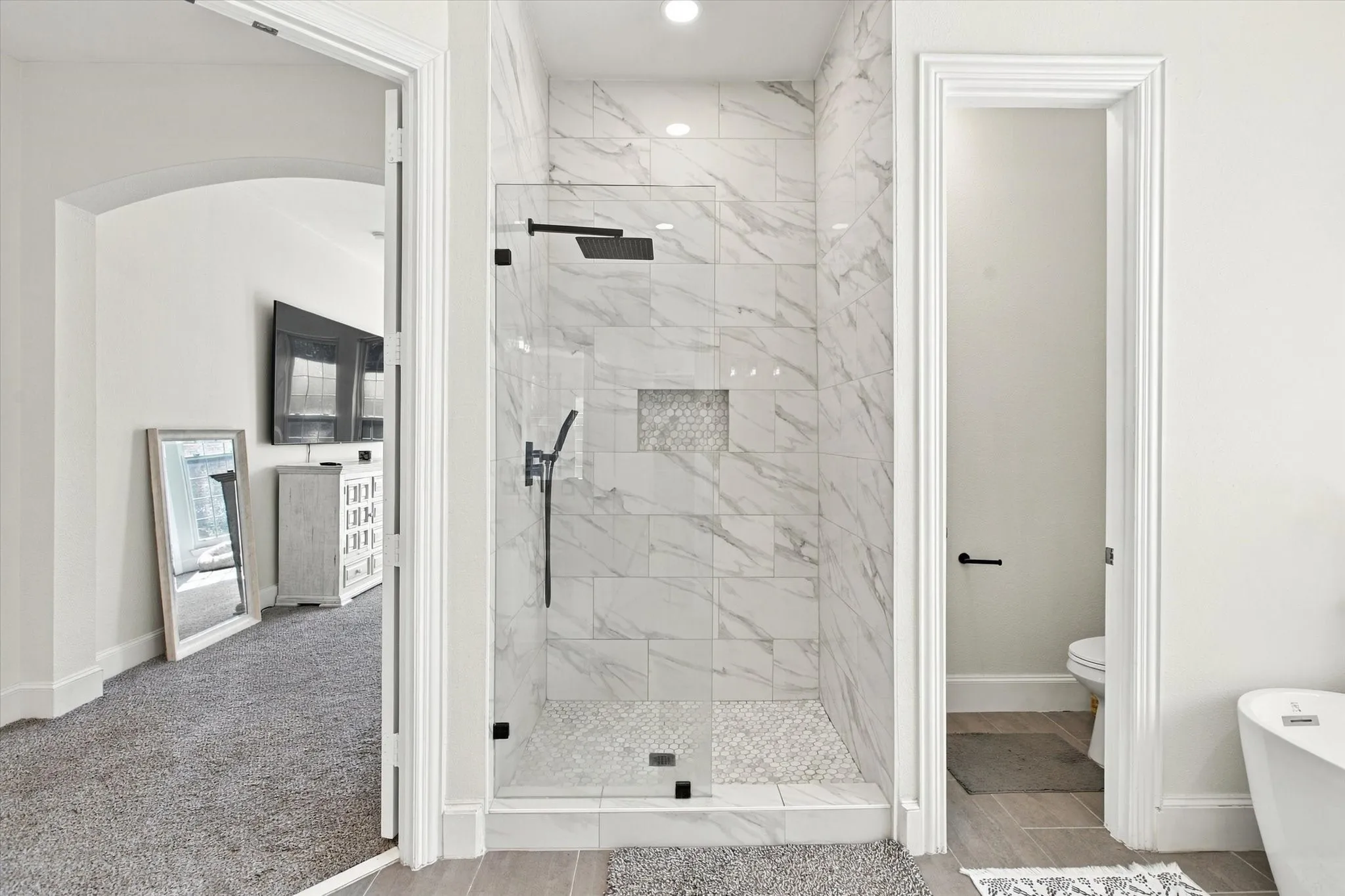 Glass-enclosed shower with full-height marble-style tile surround and recessed shelving