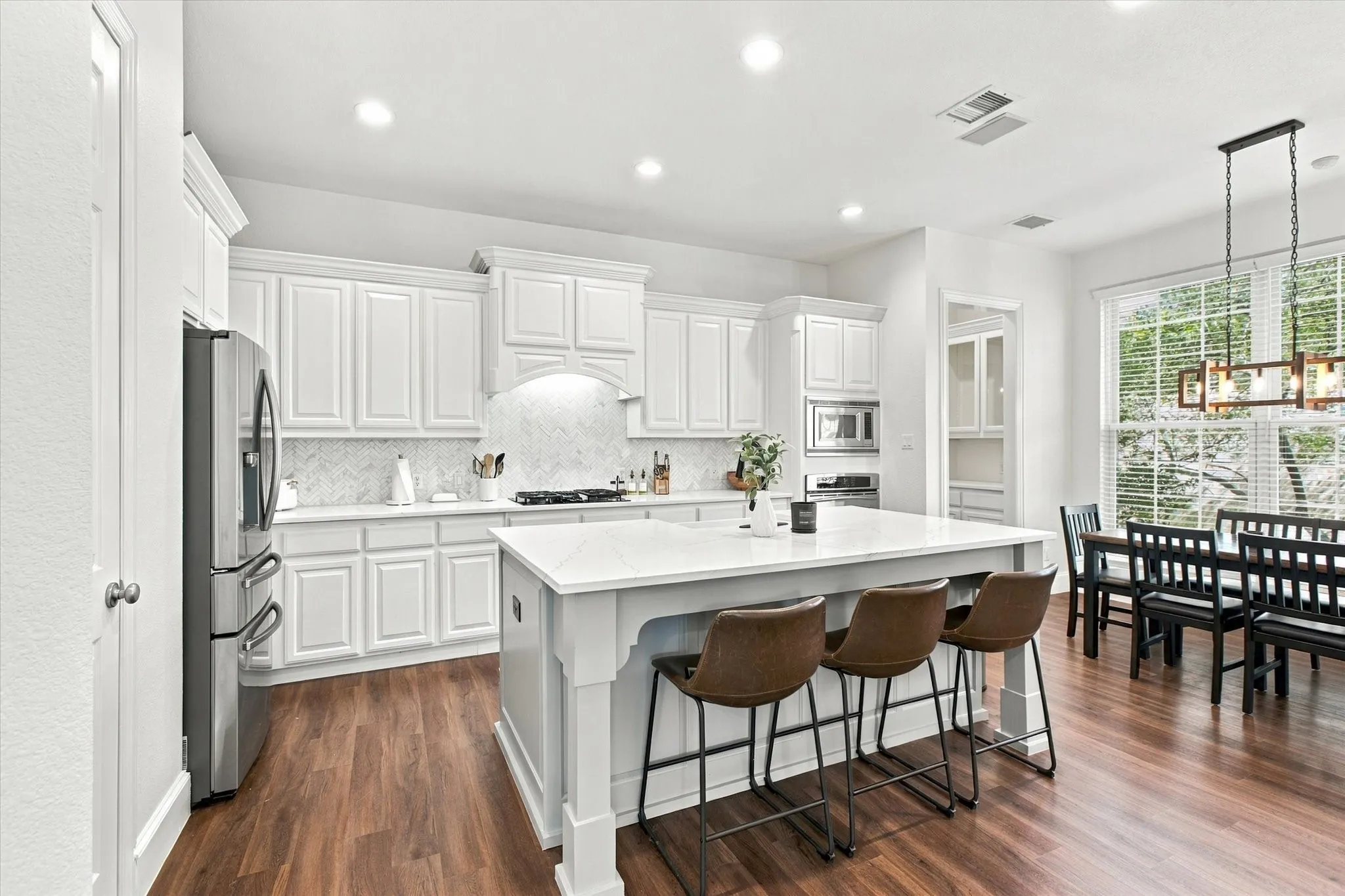 White shaker cabinetry with crown molding, stainless steel refrigerator, white subway tile backsplash, kitchen island with seating, and wood-finish flooring