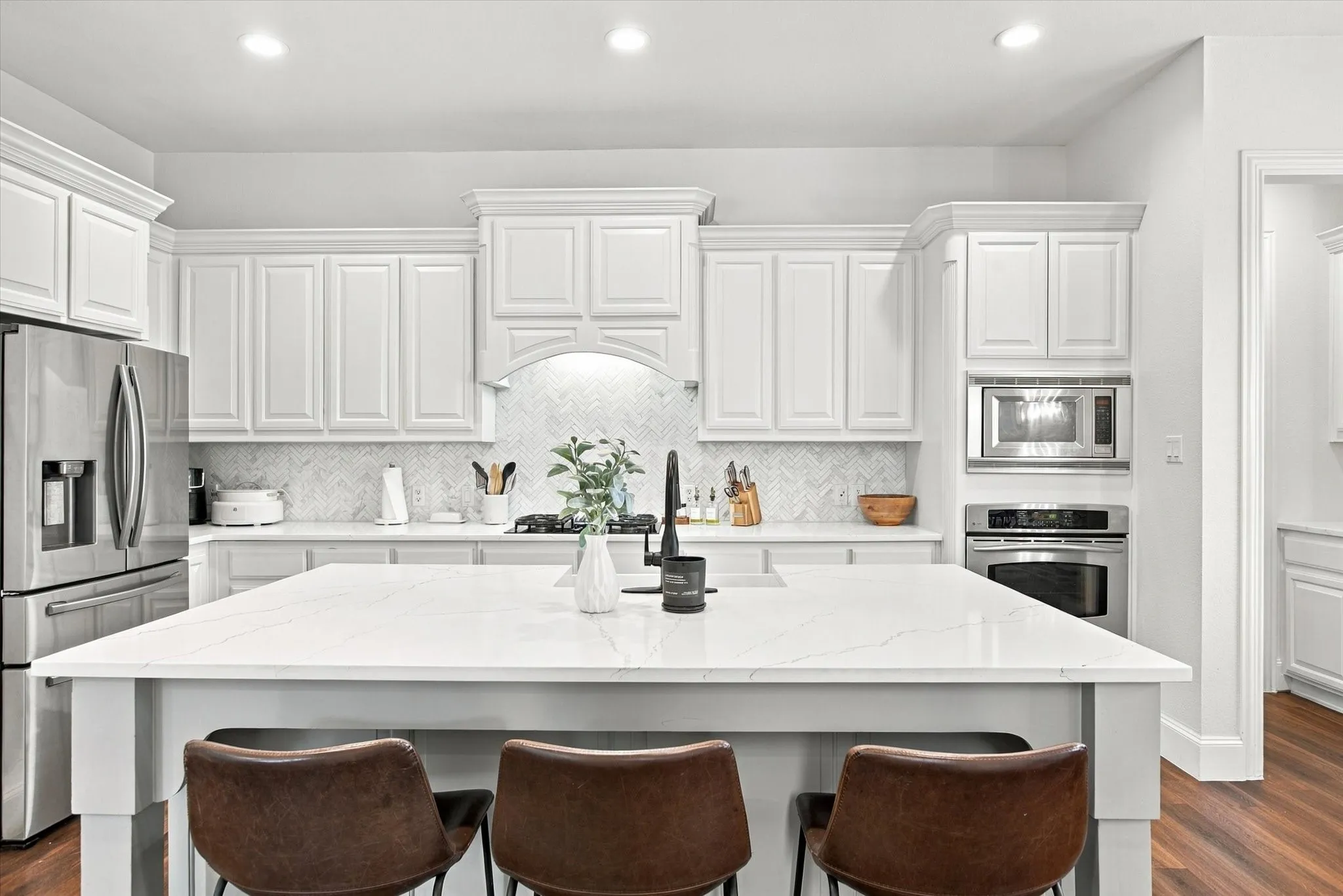 Kitchen featuring a large central island, white cabinetry with crown molding, stainless steel appliances, a tile backsplash, and recessed lighting