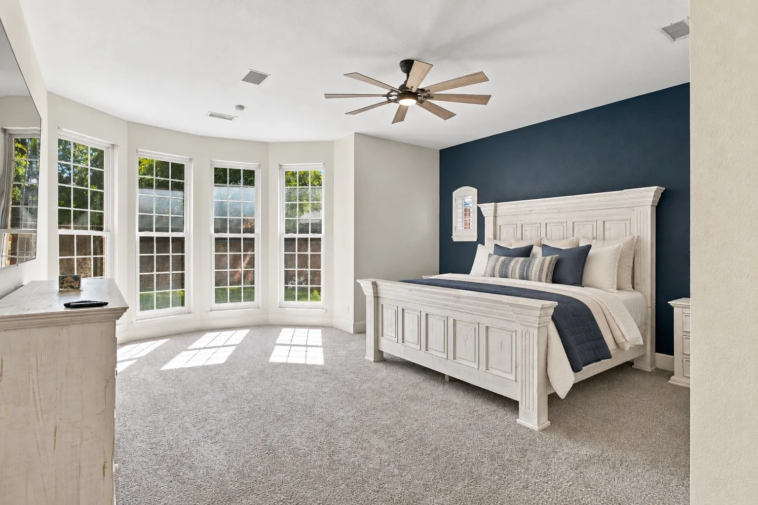 Bay window with multiple pane windows, ceiling fan with integrated lighting, neutral gray carpeting, and accent wall