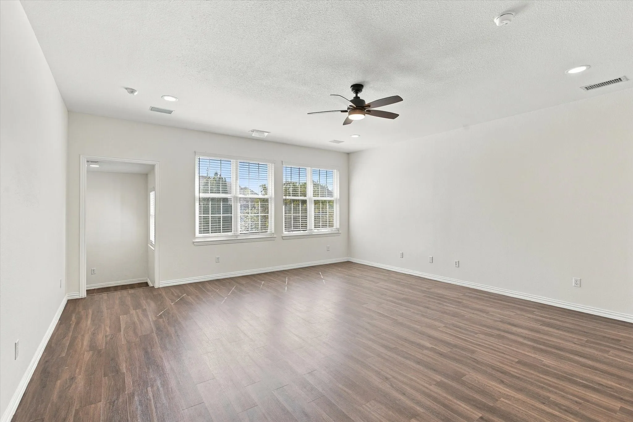 Expansive room featuring wood-finish flooring, recessed lighting, a ceiling fan, and multiple windows with white blinds