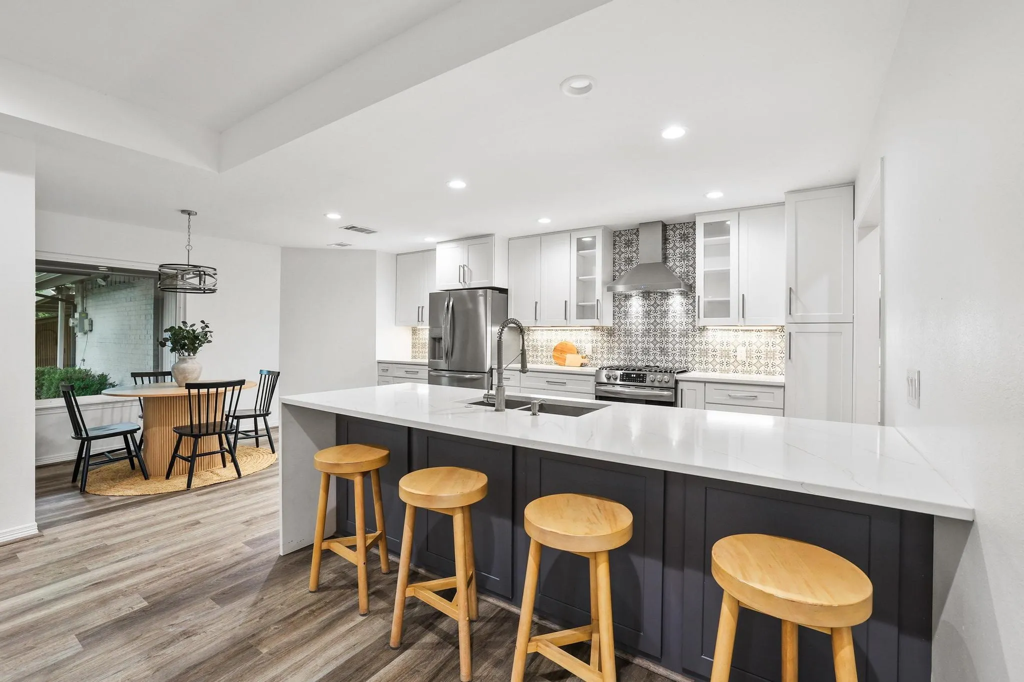 Modern kitchen featuring a large island with a light-toned countertop, white cabinetry with glass inserts, patterned backsplash, and wood-finish flooring