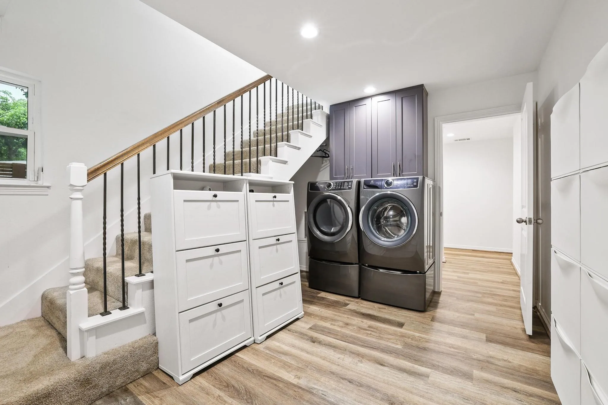 Laundry area featuring stacked washer and dryer, upper cabinetry, and wood-finish flooring