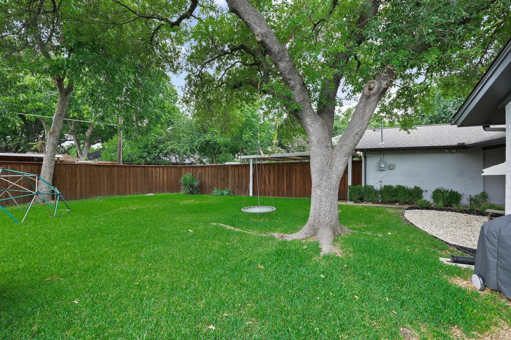 Expansive backyard featuring a manicured lawn, mature trees, wood fence, and gravel landscaping