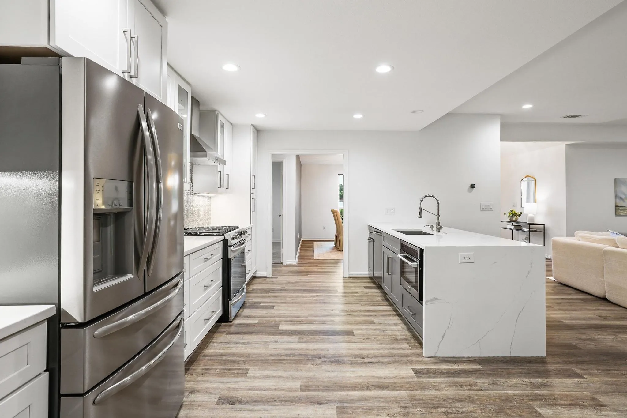 Stainless steel appliances, white cabinetry, wood-finish flooring, recessed lighting, and a kitchen island with sink