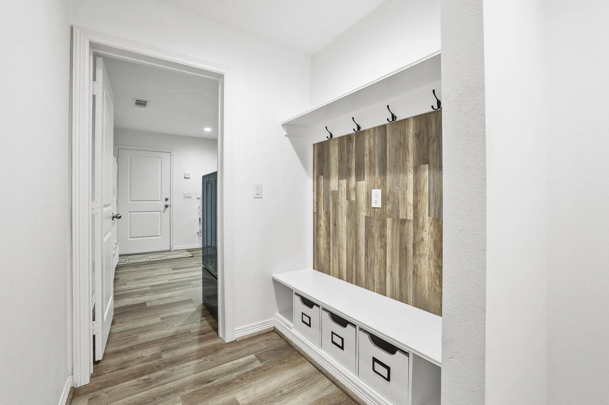Built-in mudroom bench with storage cubbies, wood-finish accent wall, and wall-mounted hooks