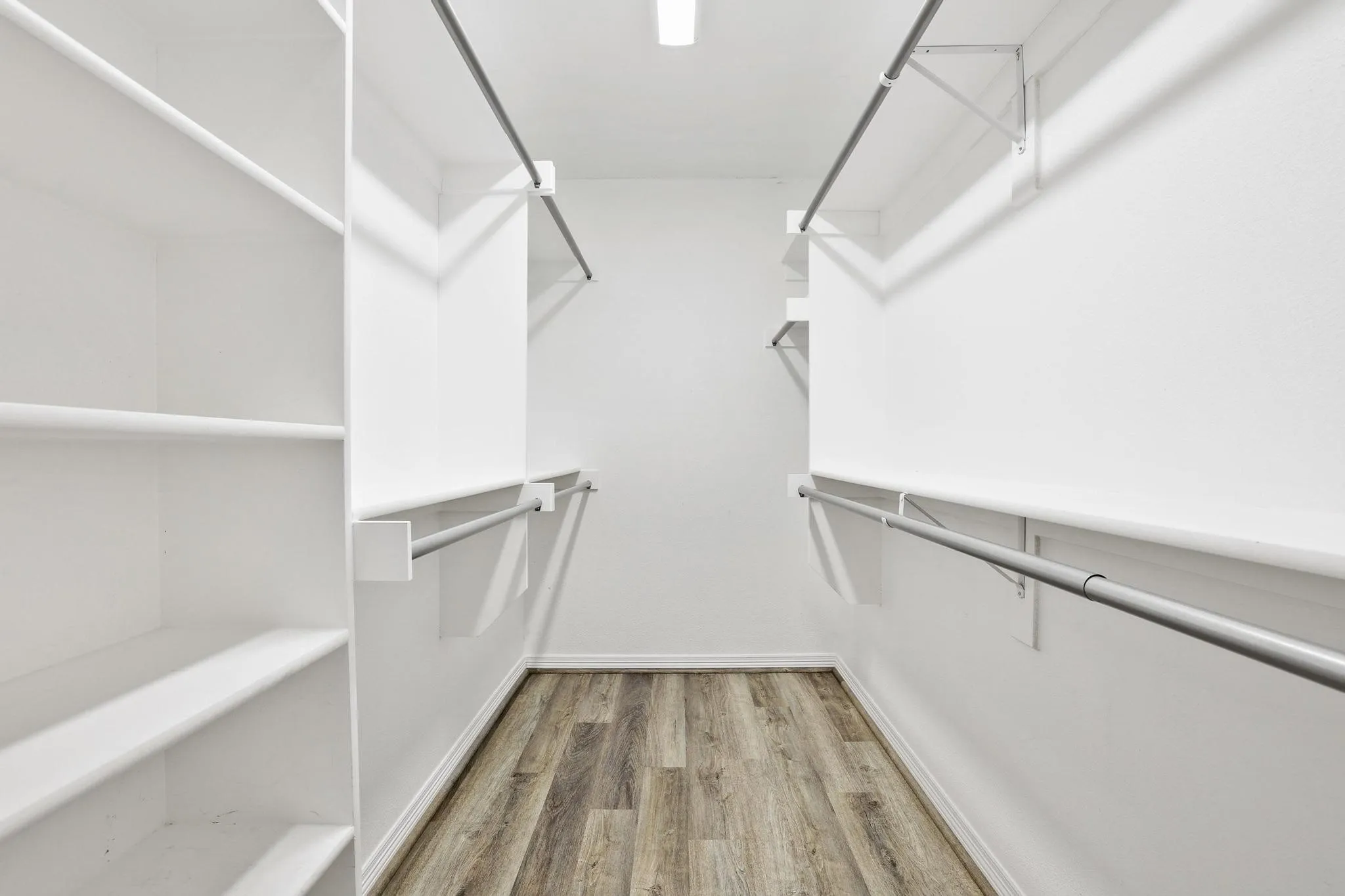 Walk-in closet featuring wood-finish flooring, built-in shelving, and multiple clothing rods
