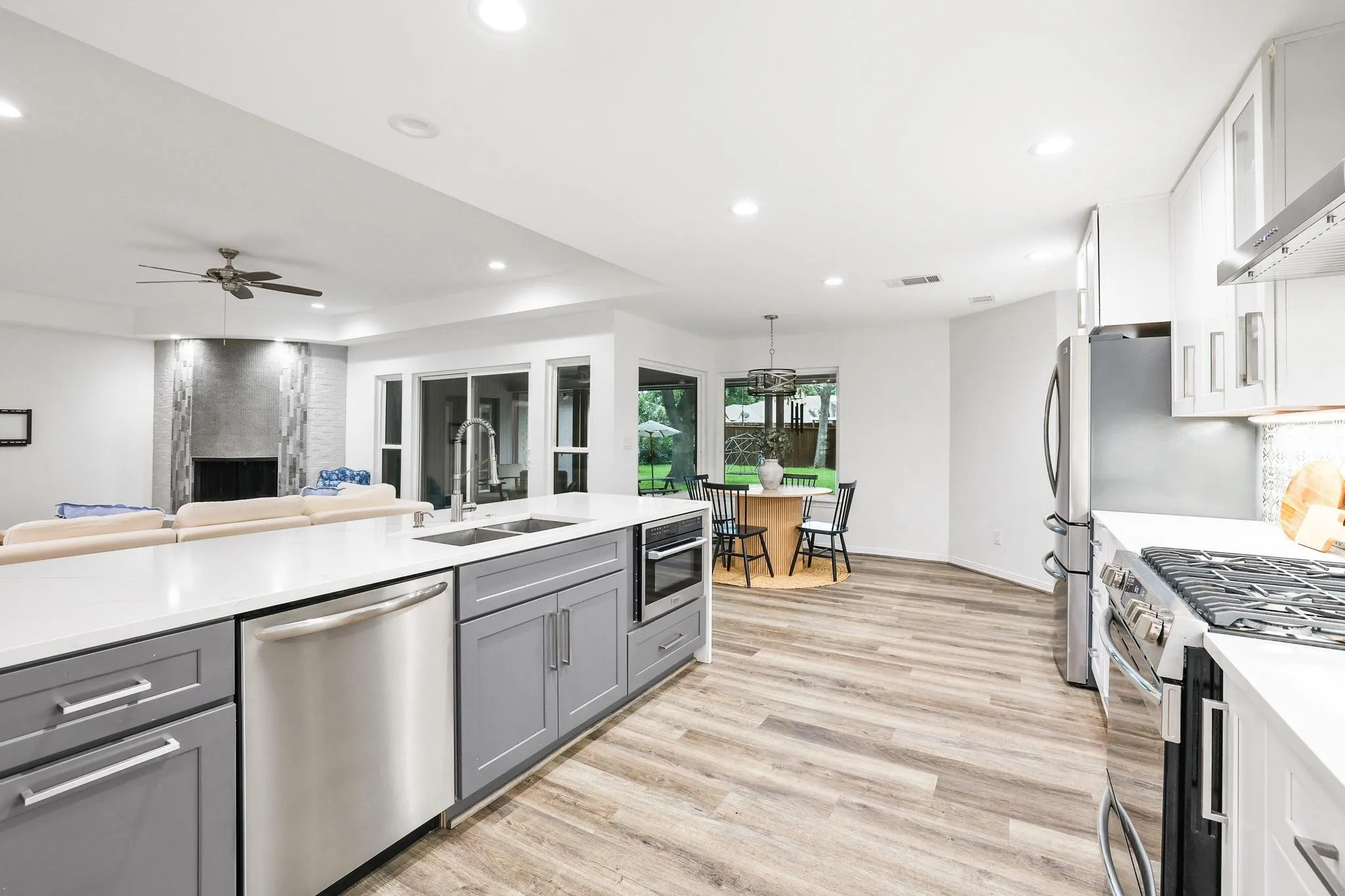 Open-concept kitchen featuring light wood-finish flooring, white countertops, stainless steel appliances, and grey cabinetry