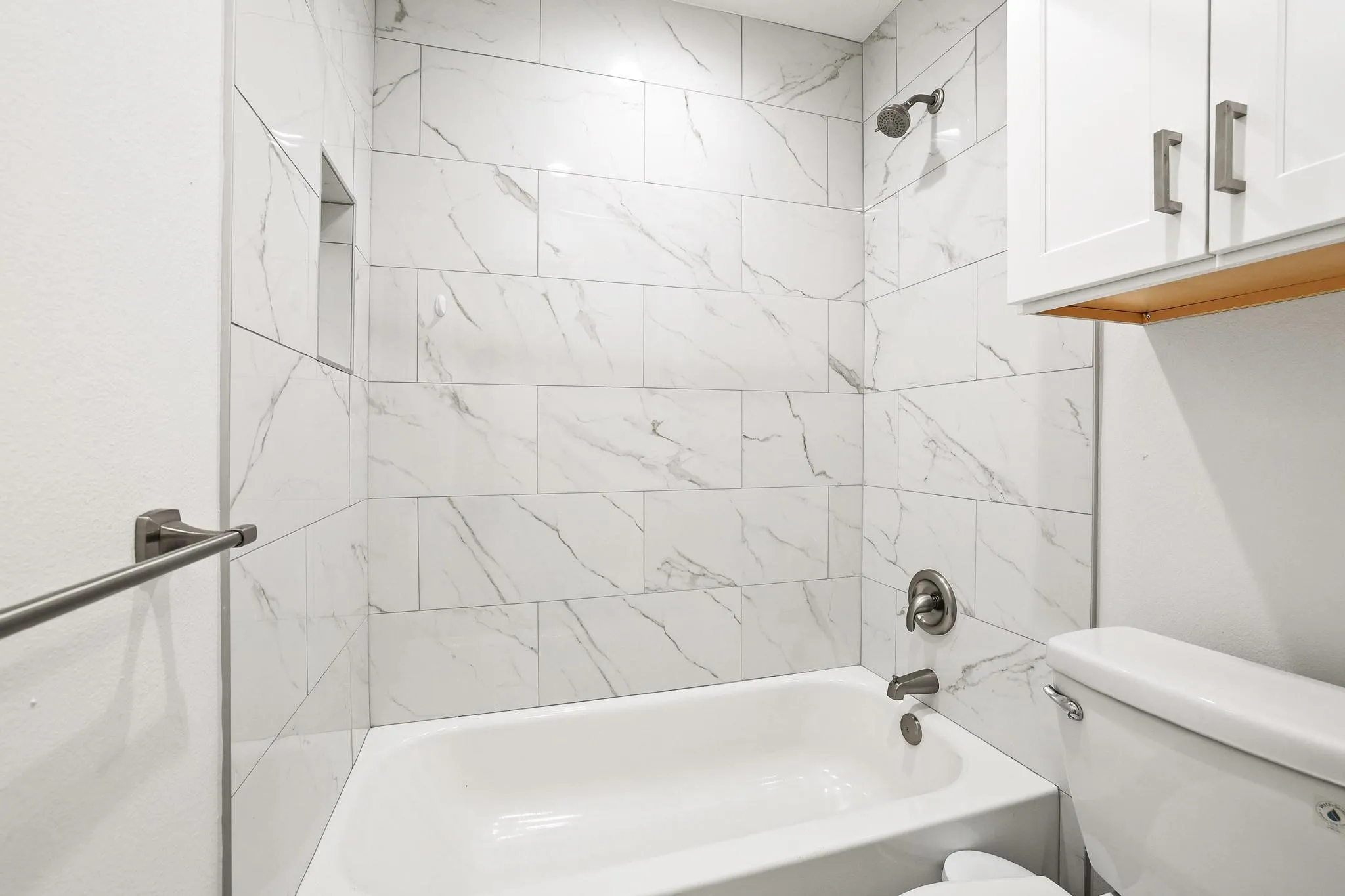 Bathtub with full-height subway tile surround, recessed shower niche, and brushed nickel fixtures