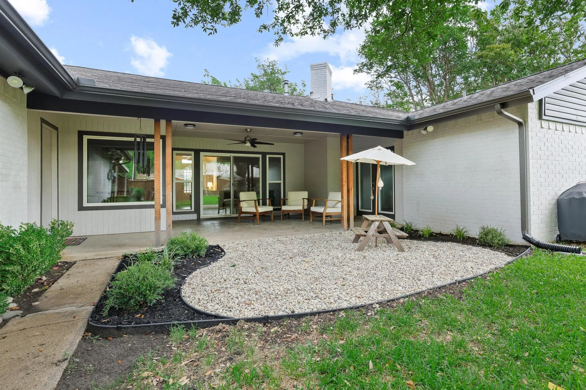 Covered patio with a concrete slab, sliding glass doors, white brick exterior, and a gravel-filled landscaping bed