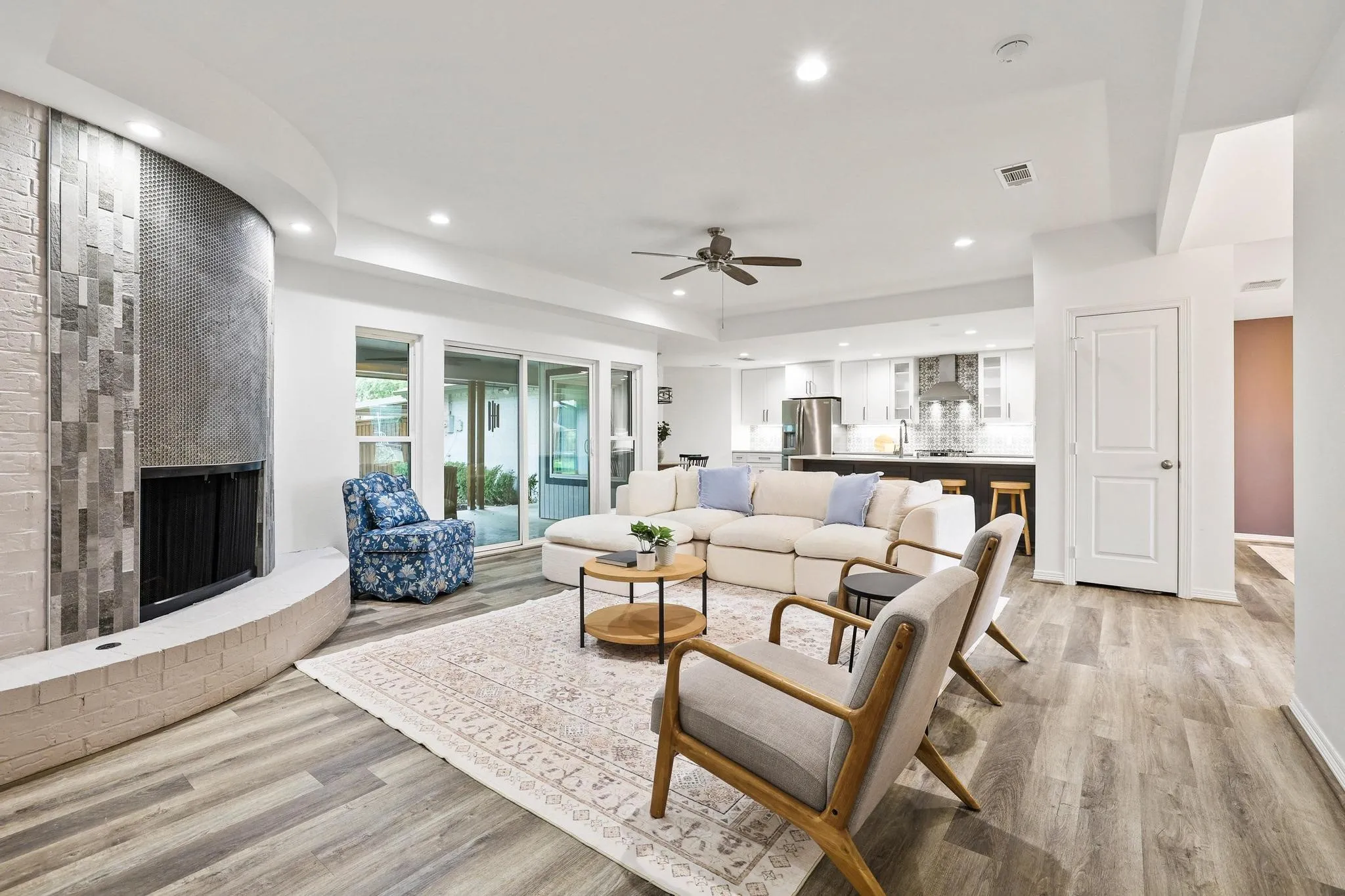 Spacious living area featuring wood-finish flooring, a curved fireplace with brick and tile accents, and recessed lighting
