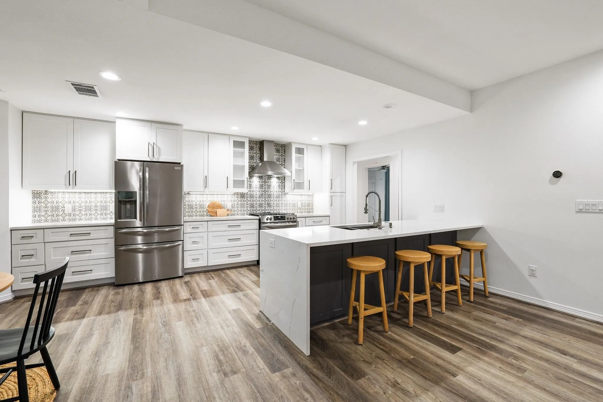 Open-concept kitchen featuring white cabinetry, stainless steel appliances, patterned backsplash, an island with a built-in sink, and wood-finish flooring