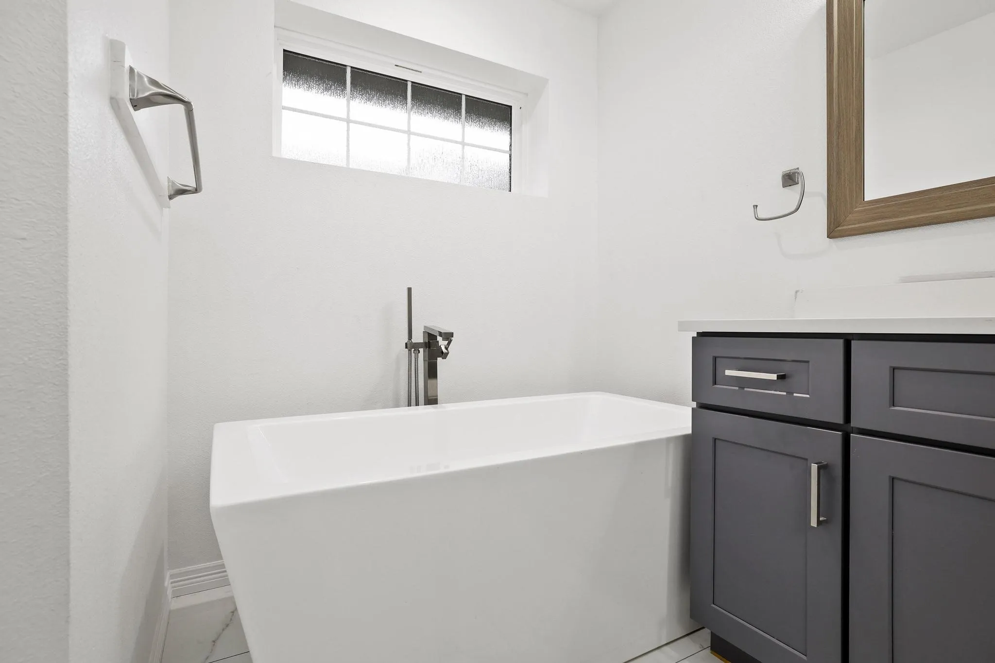 Freestanding soaking tub with a floor-mounted faucet, dark gray vanity cabinetry, and a framed mirror