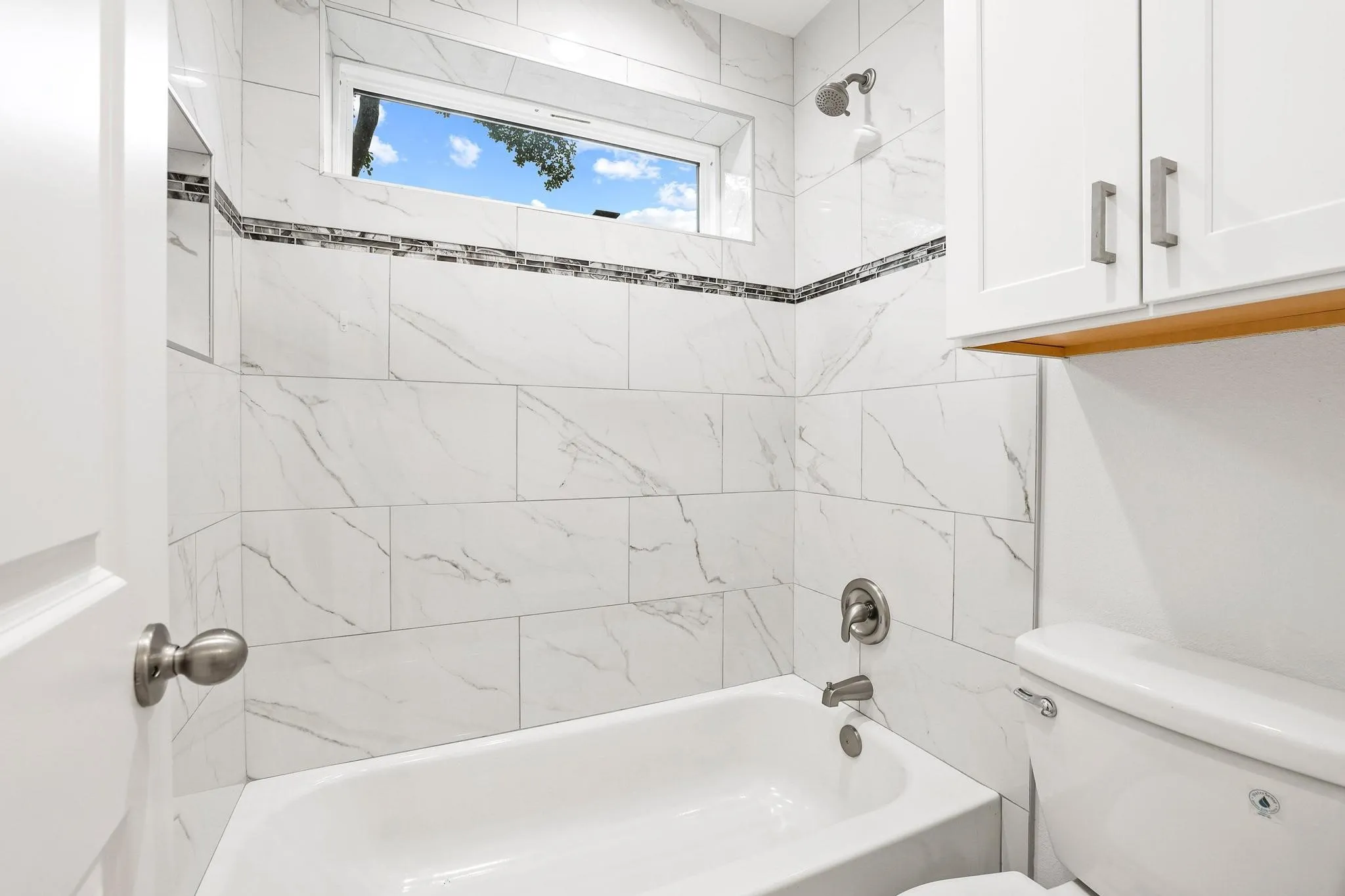 Bathtub with white subway tile surround and decorative mosaic accent